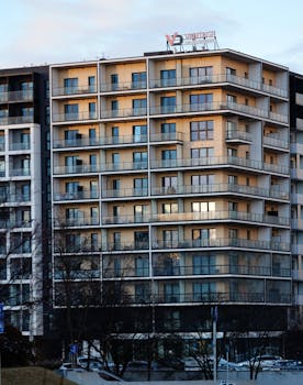 A contemporary multi-story apartment building with balconies and a visible logo captured at sunset.