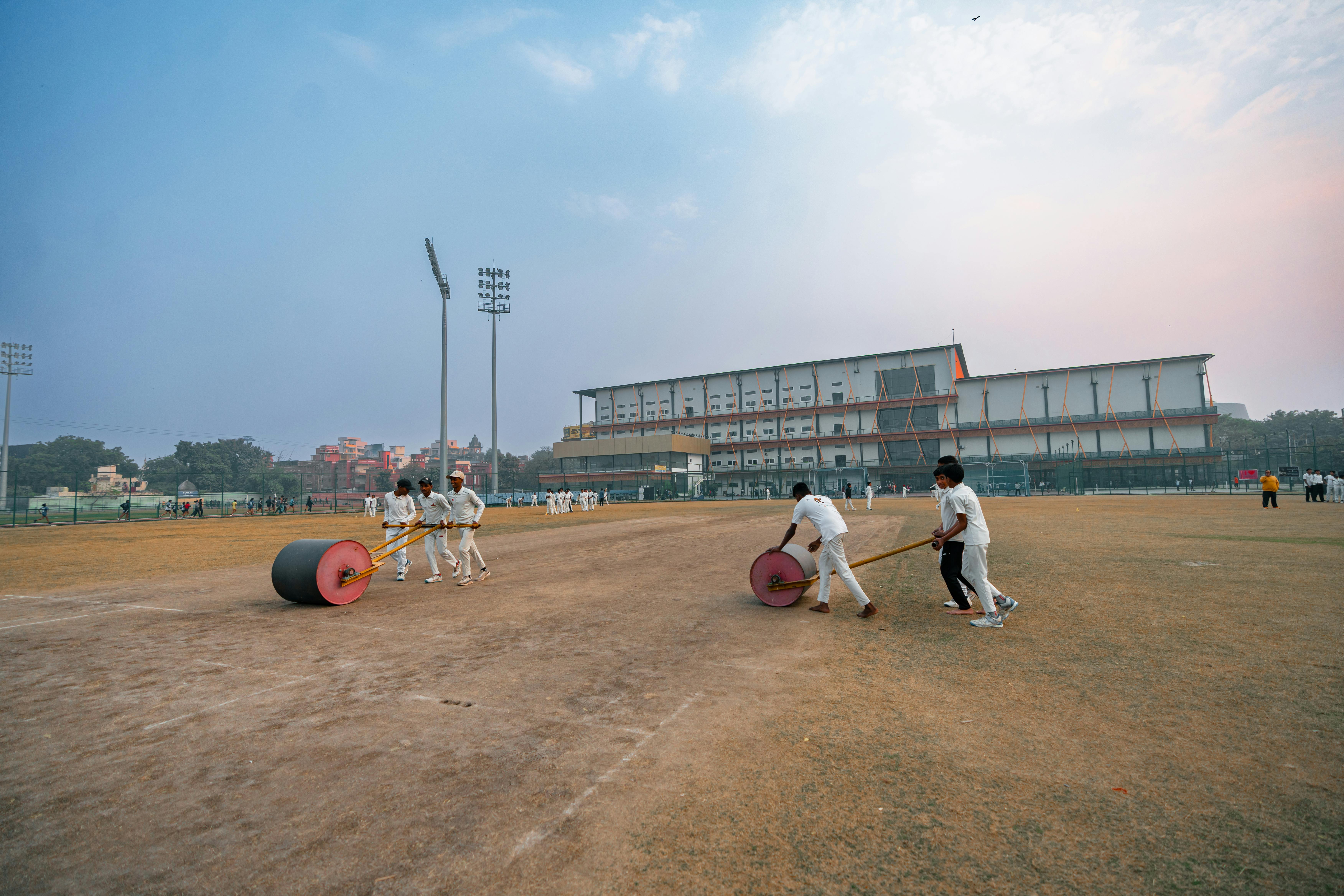 無料 日没時に、インドのデリーでグラウンドキーパーがローラーを使ってクリケット場を整備している。 写真素材