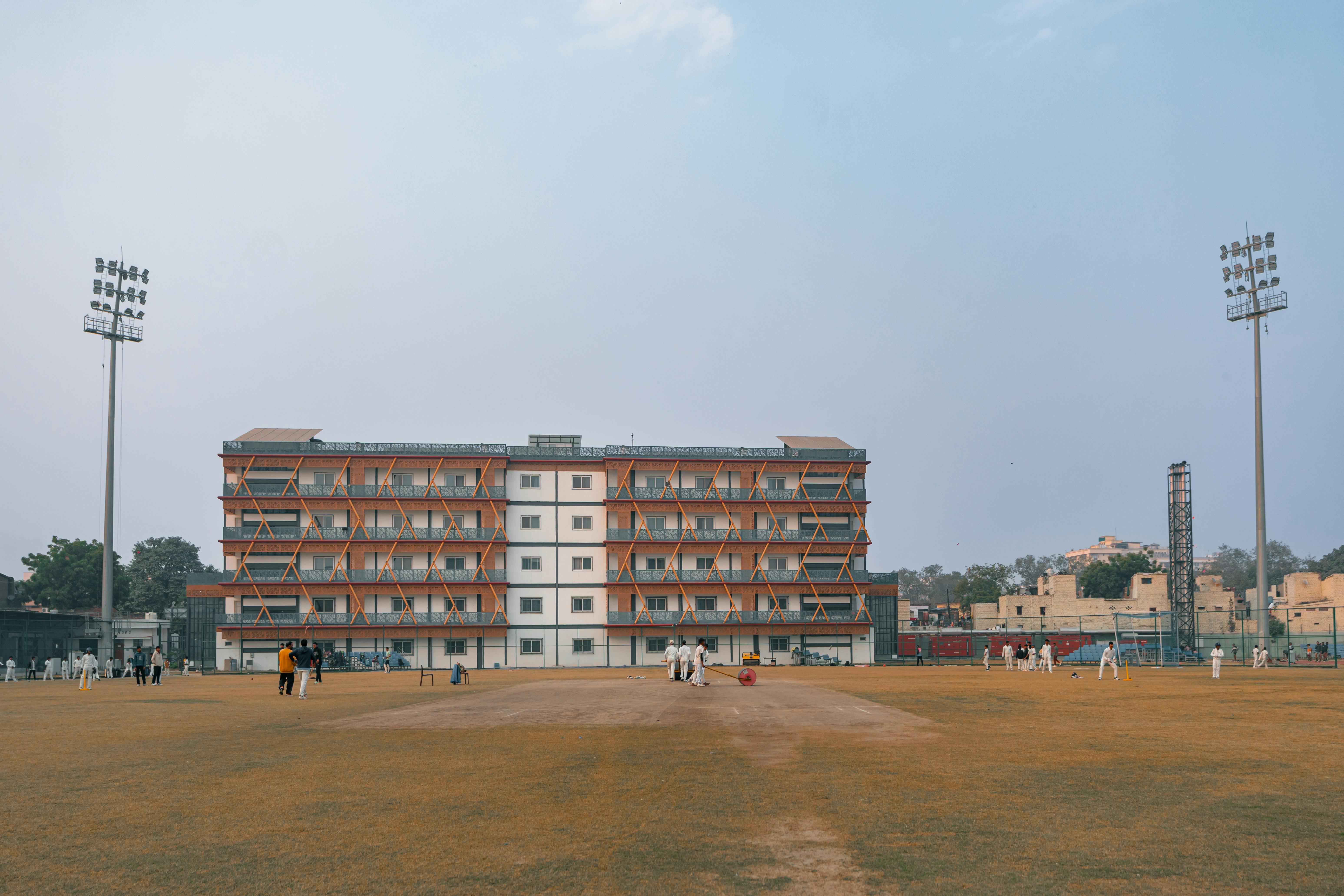 Gratis Cricketkamp på dagtid på en stor idrettsbane i Delhi, India med spillere og flomlys. Arkivbilde