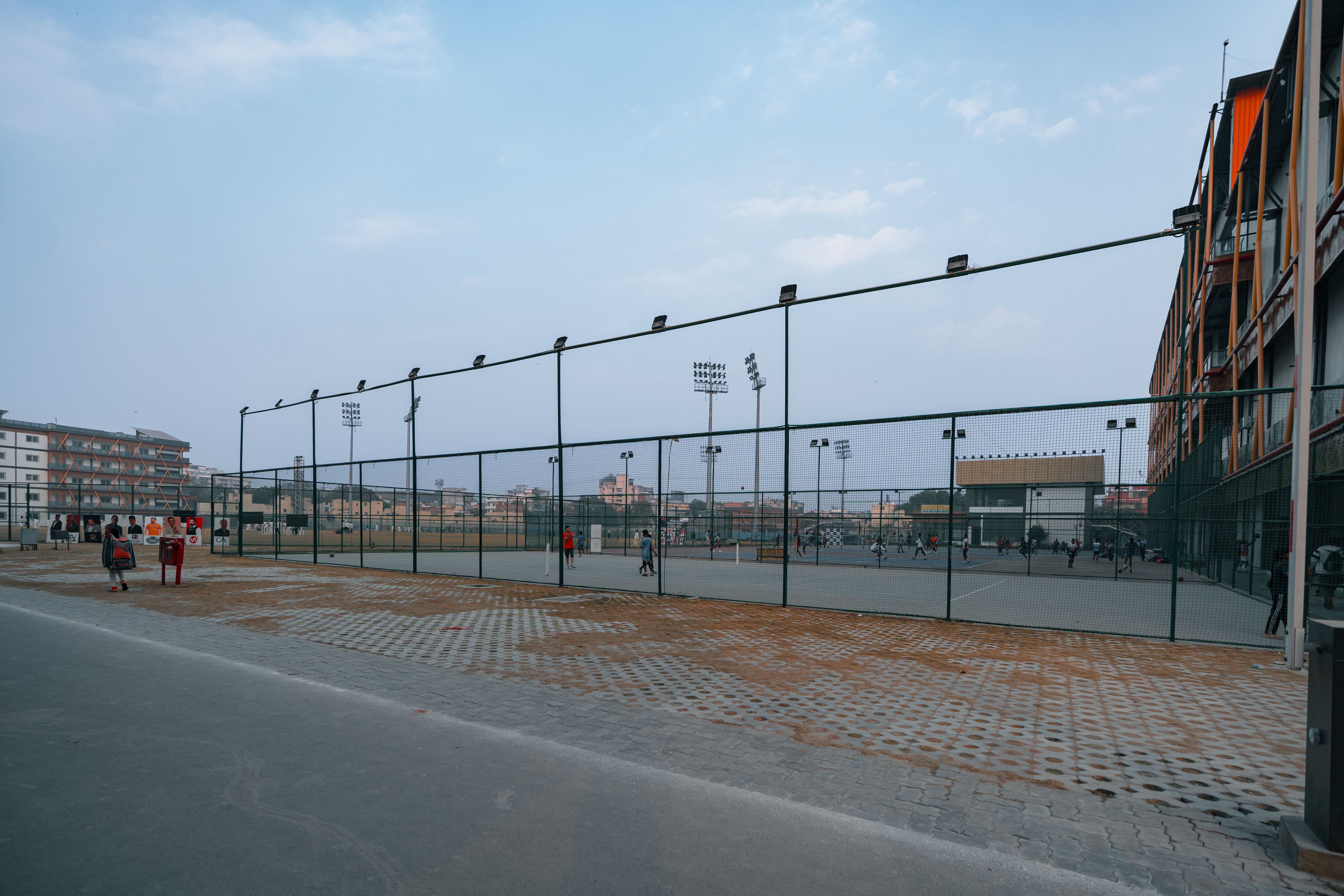 Wide view of a sports complex in Delhi, India, showcasing tennis courts and floodlights under a clear sky.