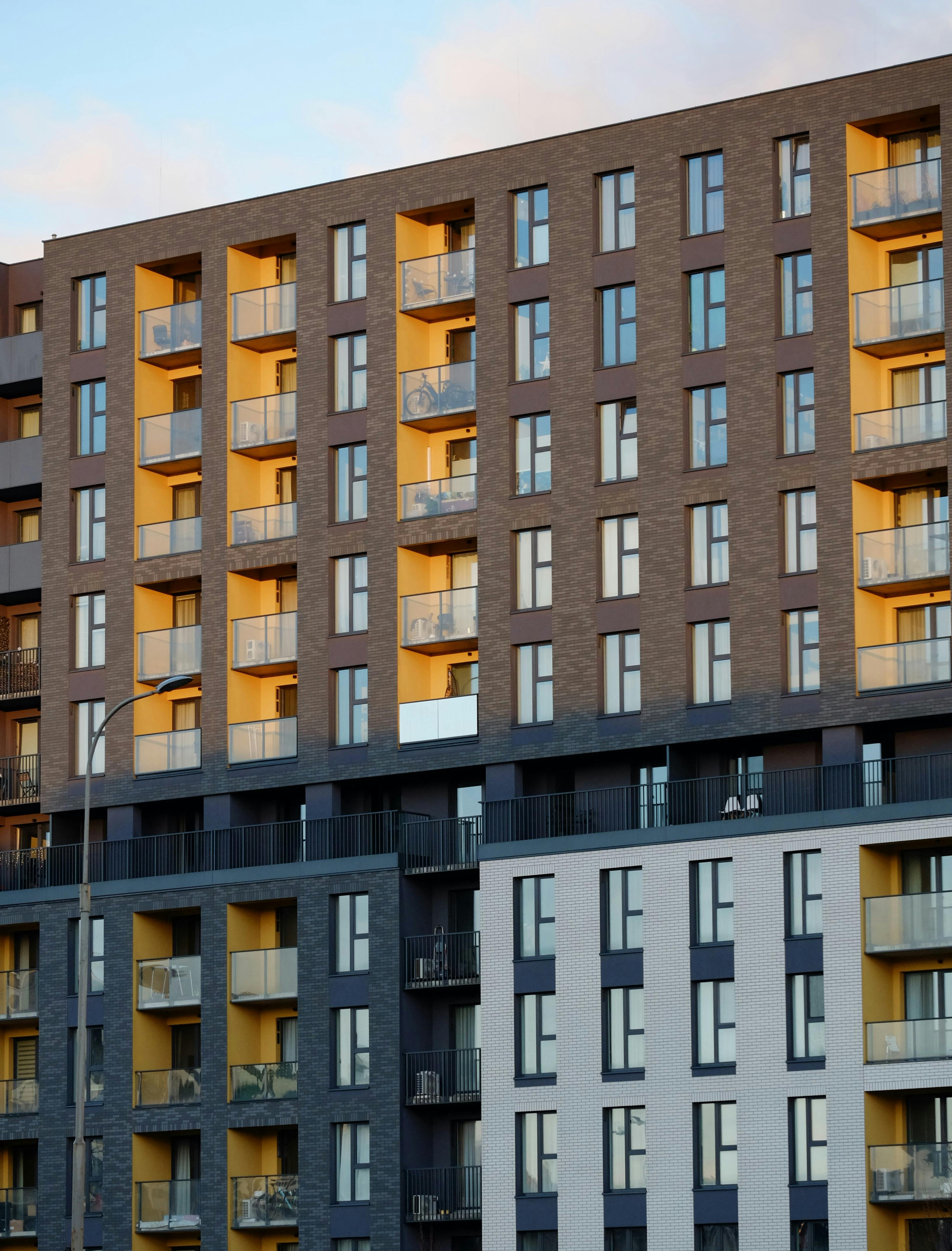 бесплатная Современный жилой комплекс со стеклянными балконами и подсветкой, имитирующей закат, подчеркивает архитектурный стиль. Стоковое фото