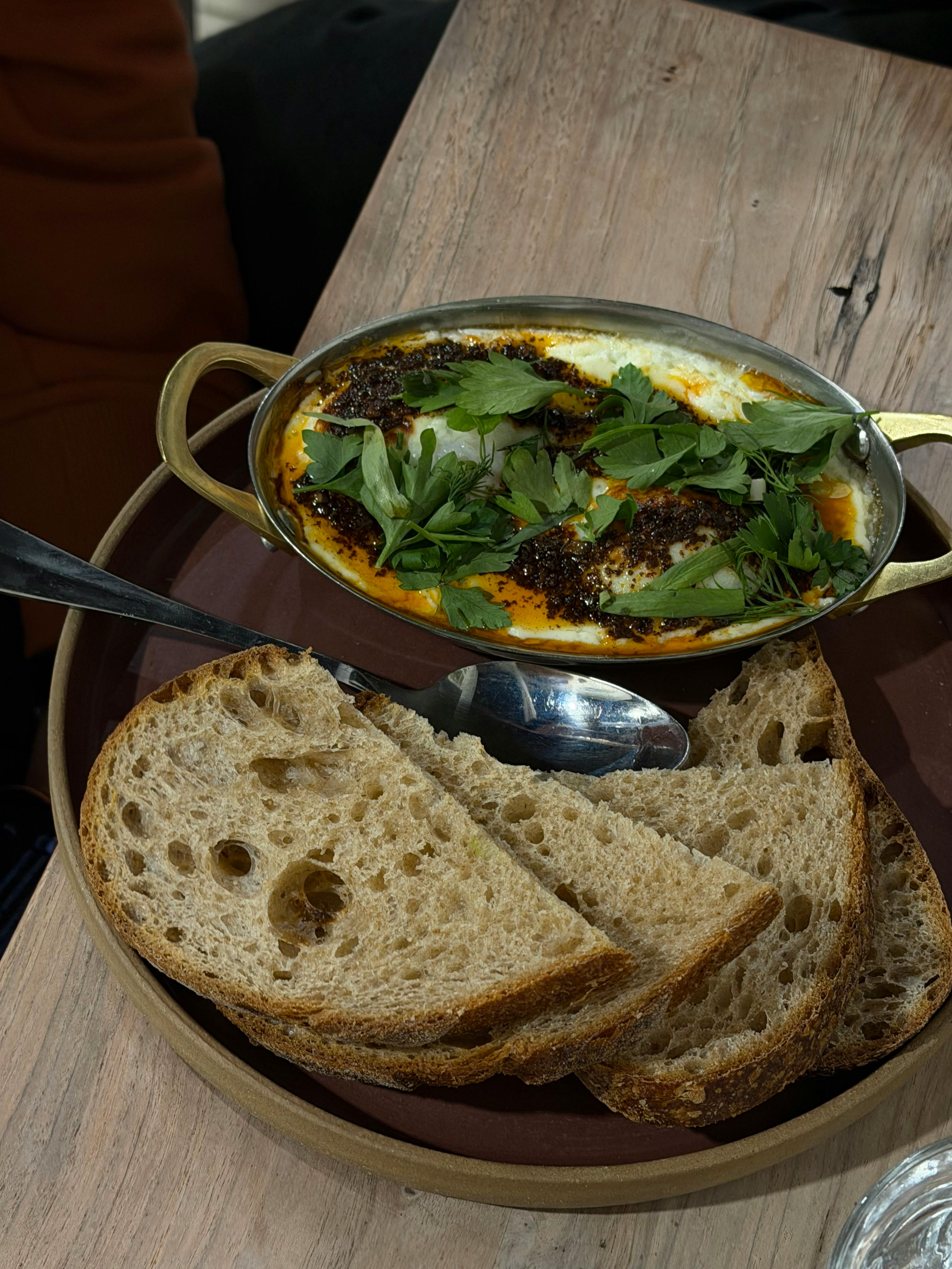 Gratis Shakshuka yang menggugah selera disajikan dengan irisan roti tawar di atas meja kayu, sempurna untuk santapan mewah. Foto Stok