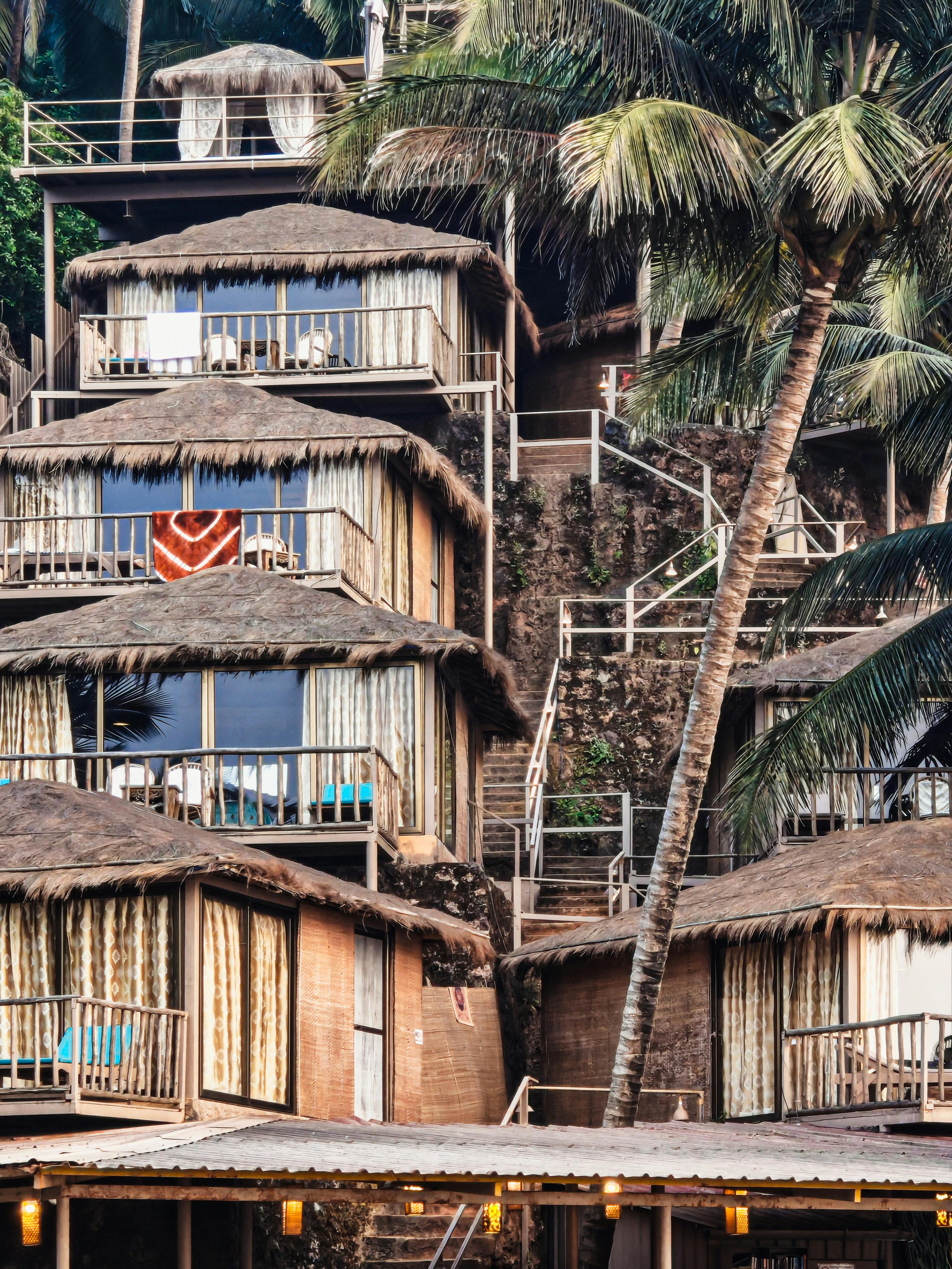 Gratis Gubuk-gubuk bambu yang menawan terletak di tengah rimbunnya pohon palem, menawarkan tempat peristirahatan tropis yang tenang. Foto Stok
