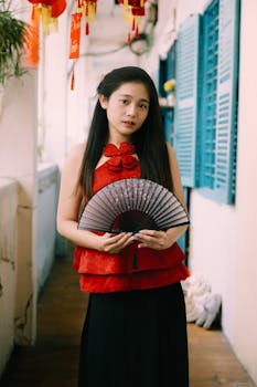 A woman in a red dress holds a fan, standing in a decorated corridor.