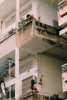 Urban scene with two people engaging across concrete balconies, showcasing city life dynamics.