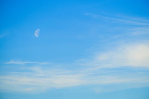 Free A serene view of the crescent moon against a bright blue sky with wispy white clouds. Stock Photo