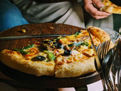 Delicious vegetarian pizza with toppings of olives, bell peppers, and more on a wooden platter.