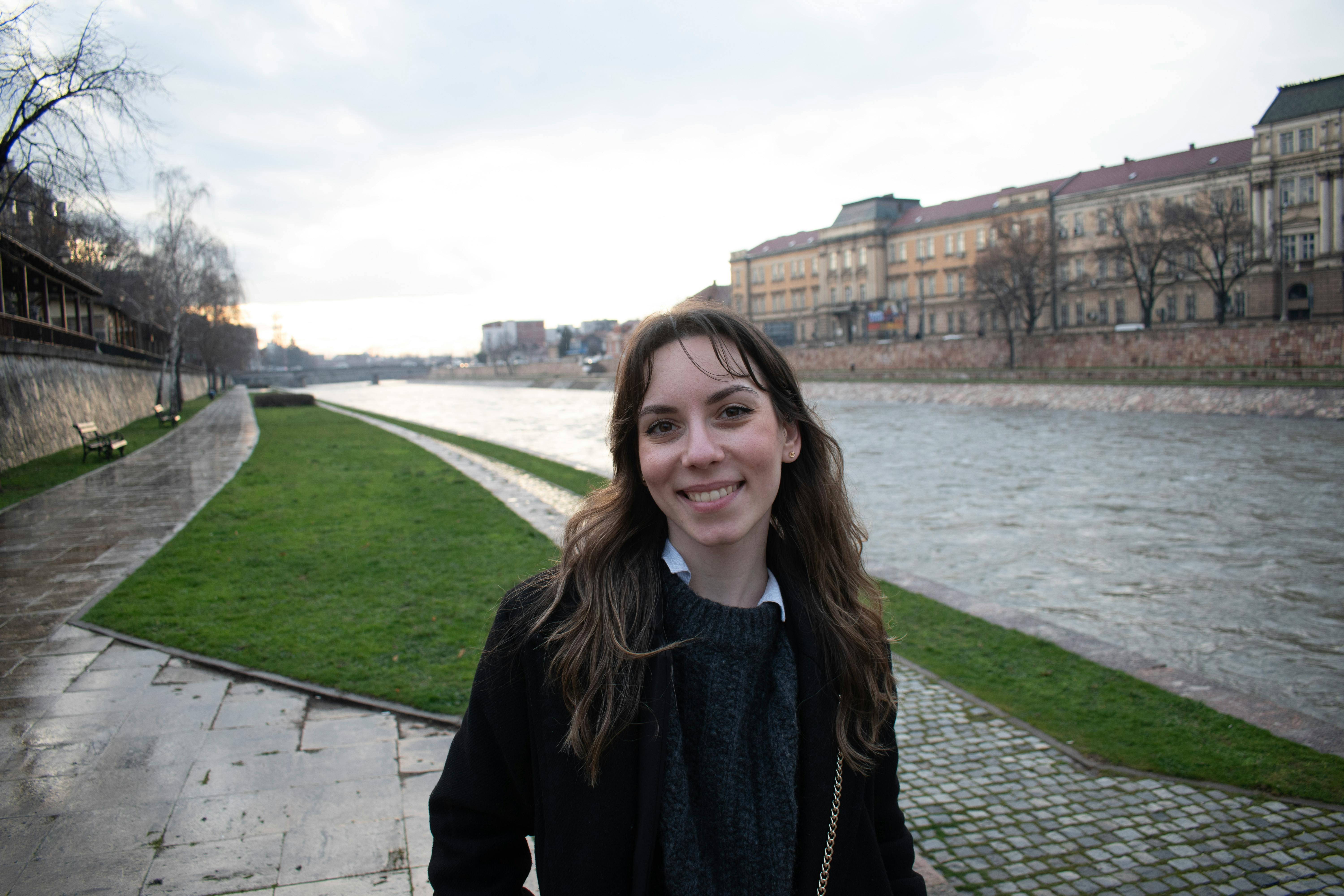 Gratis Seorang wanita tersenyum di tepi Sungai Danube di Belgrade, Serbia, pada hari yang mendung. Foto Stok