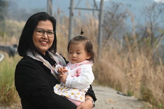 Smiling mother holding baby outdoors in a serene autumn landscape.
