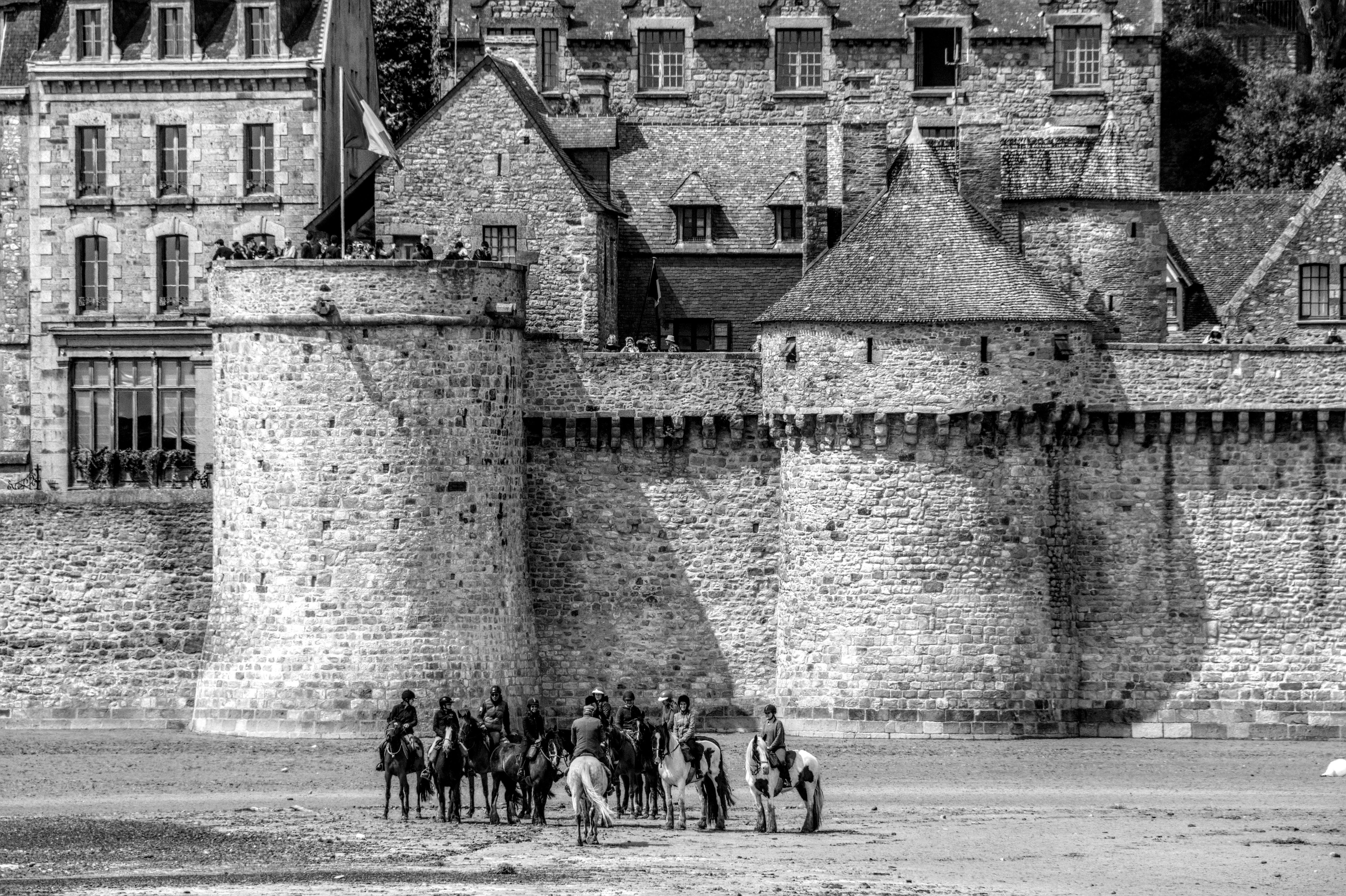 бесплатная Средневековая каменная крепость в Бретани с всадниками на песчаном переднем плане, демонстрирующая историческую архитектуру. Стоковое фото