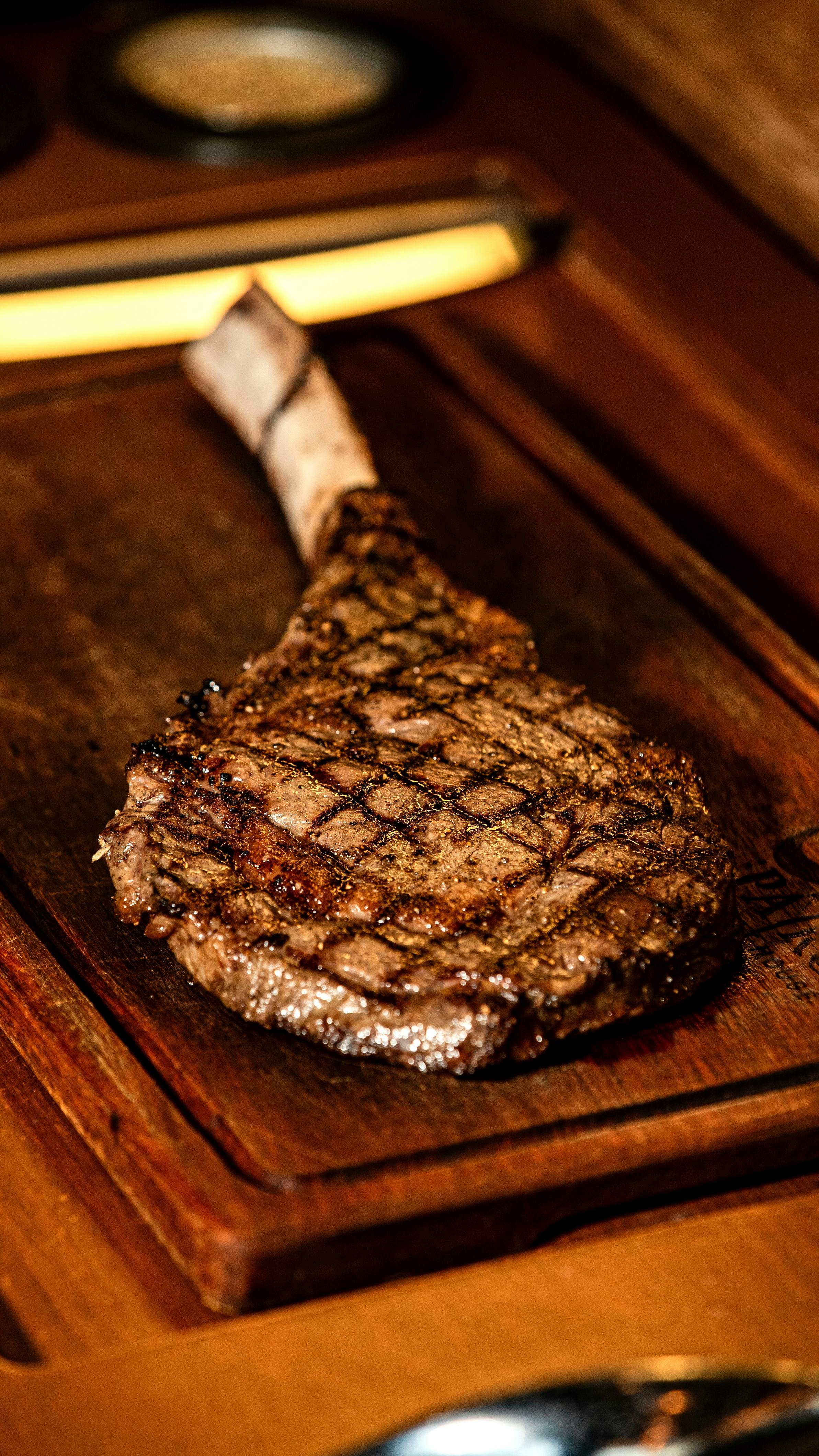 Gratis Steak tomahawk yang dipanggang sempurna diletakkan di atas papan saji kayu, memperlihatkan teksturnya yang juicy. Foto Stok