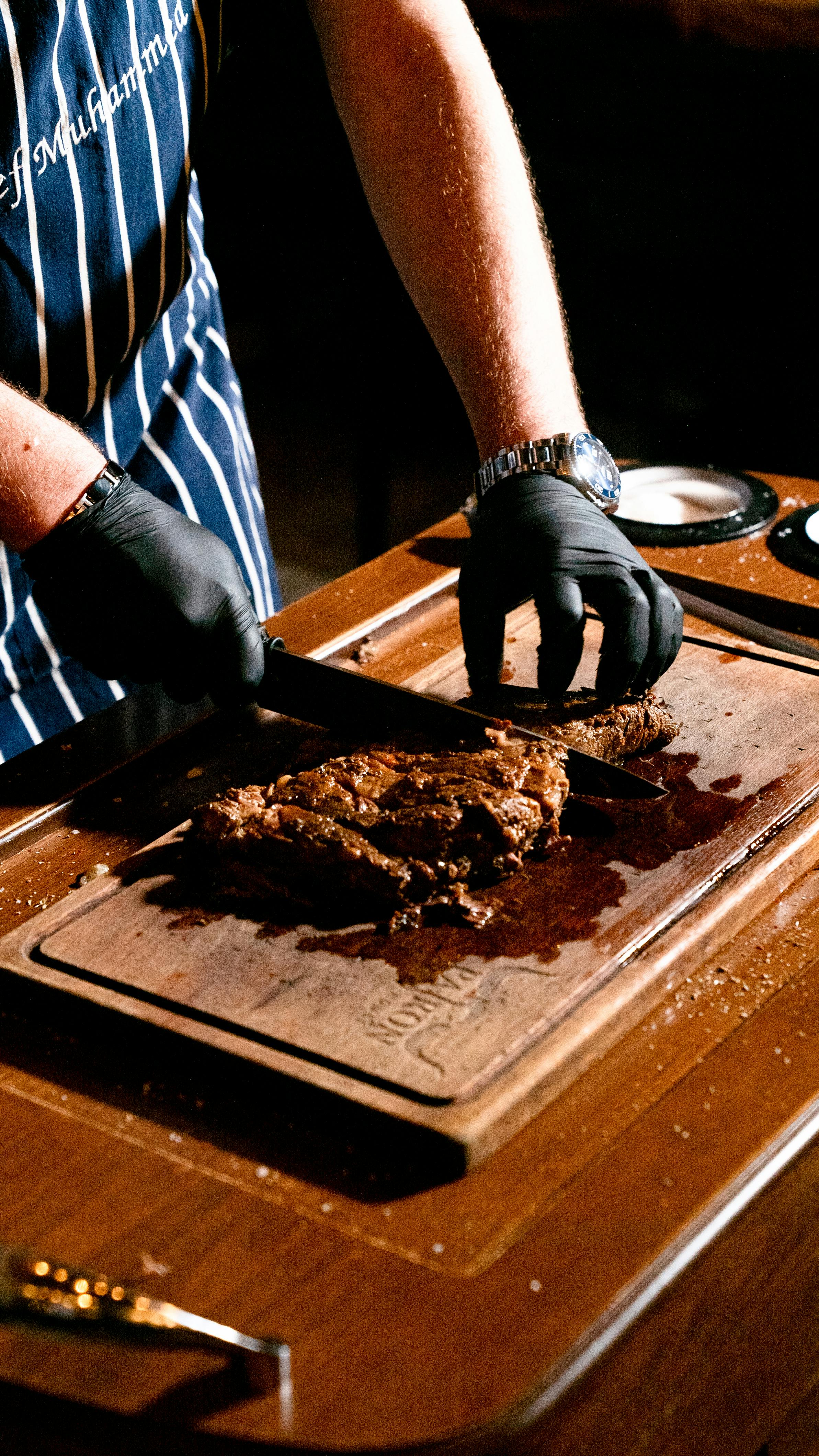 Gratis En kokk skjærer kyndig en saftig biff på et skjærebrett av tre innendørs. Arkivbilde