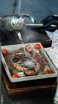 Juicy grilled steak with broth poured over, surrounded by cherry tomatoes, creating a gourmet culinary scene.
