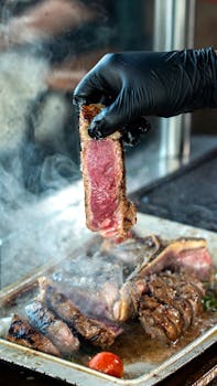 Close-up of grilled steak slice lifted with glove over smoky grill.