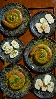 Overhead view of spiral pastries and cheese on black plates, garnished with herbs.