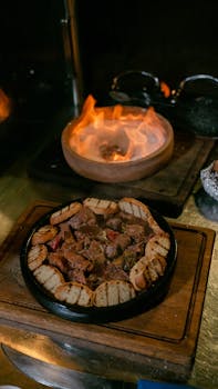 A savory grilled meat platter with bread slices served on a wooden board, featuring a fiery background.