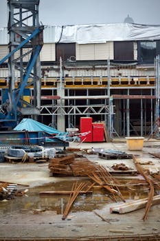 Industrial construction site with scattered materials and equipment on a rainy day.