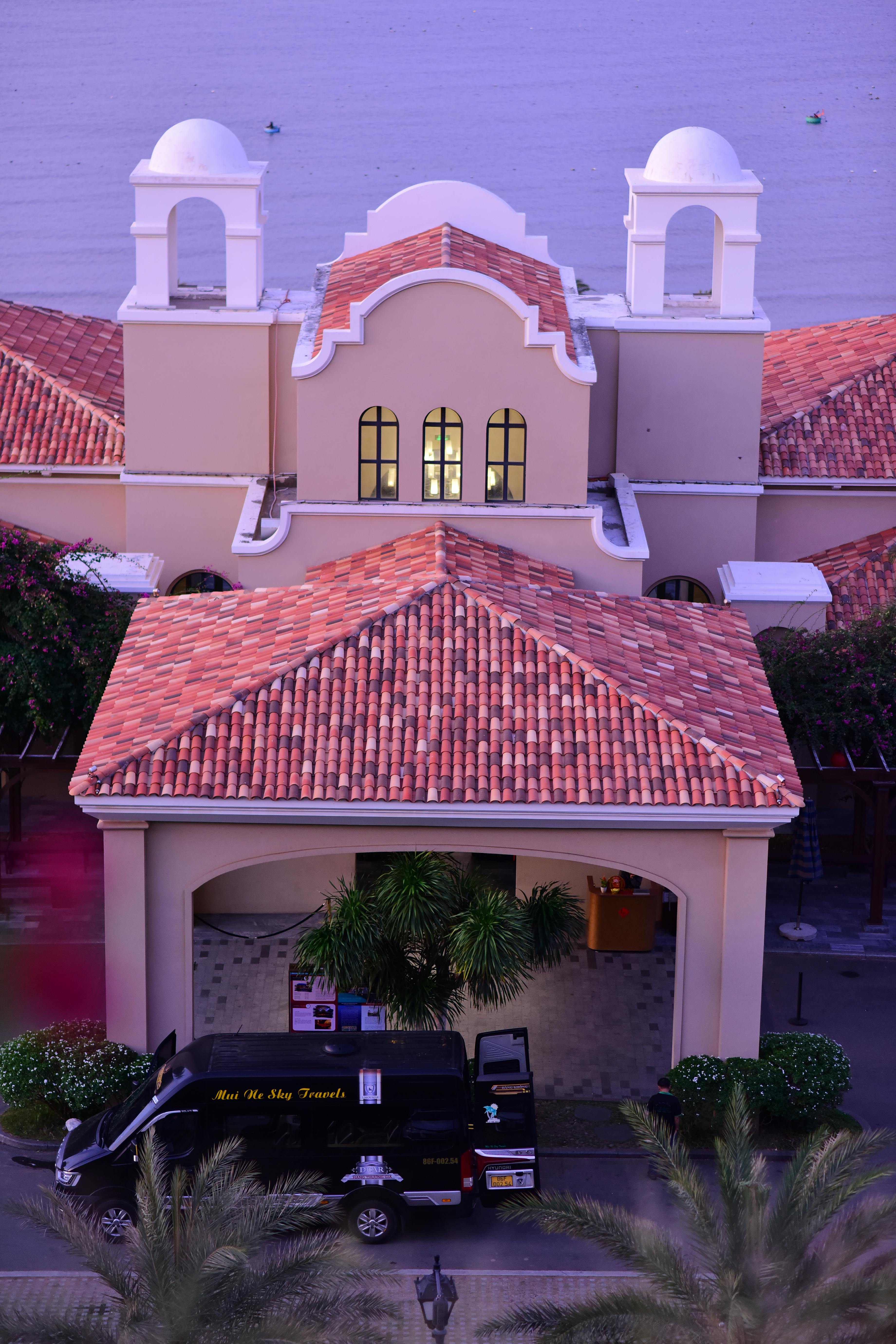 無料 赤い瓦屋根のコロニアル様式の建物と、その外に駐車されたバンの航空写真。建築の美しさが際立っています。 写真素材