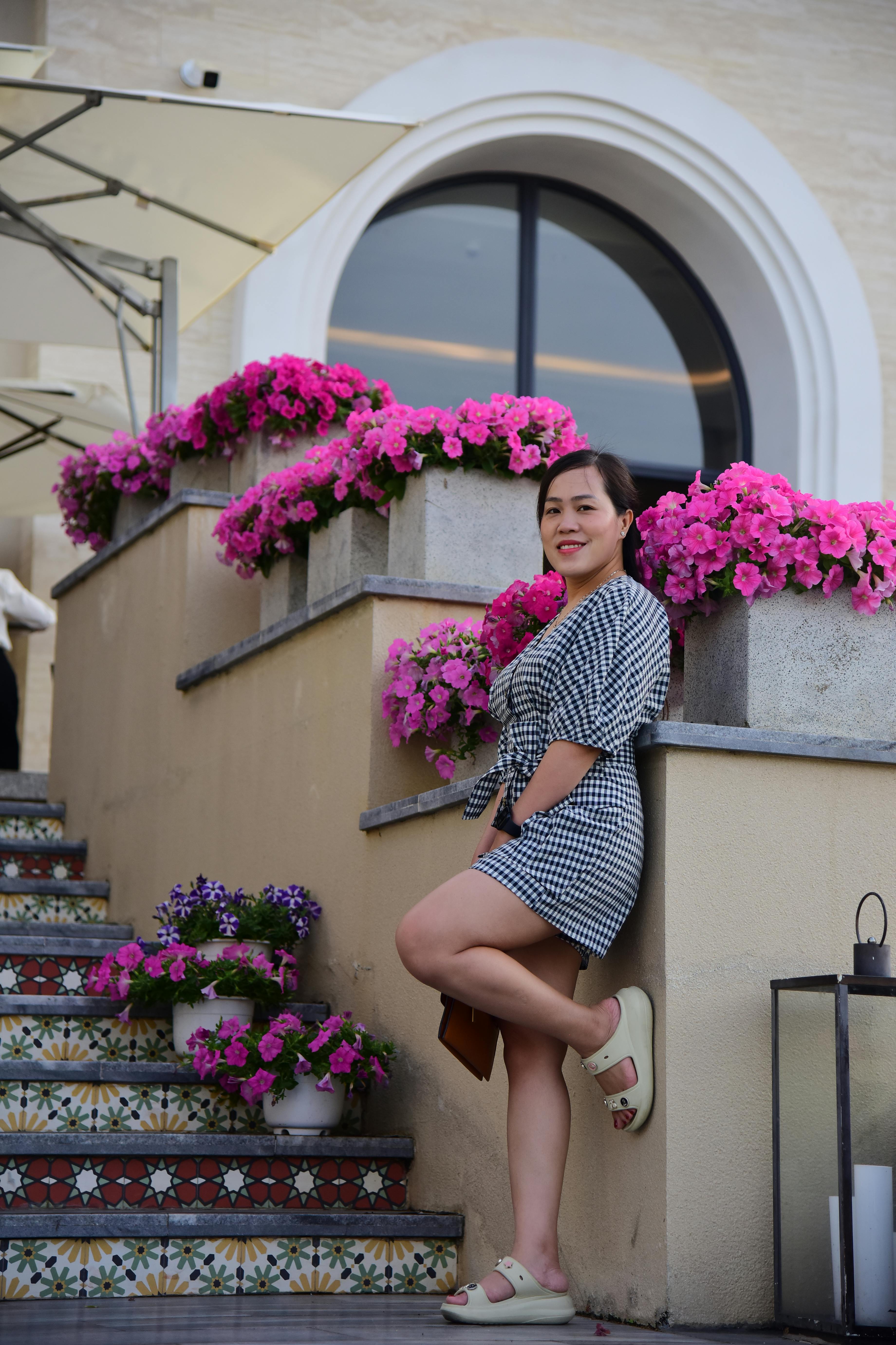 бесплатная Женщина в клетчатом платье наслаждается моментом на террасе, украшенной цветами. Стоковое фото