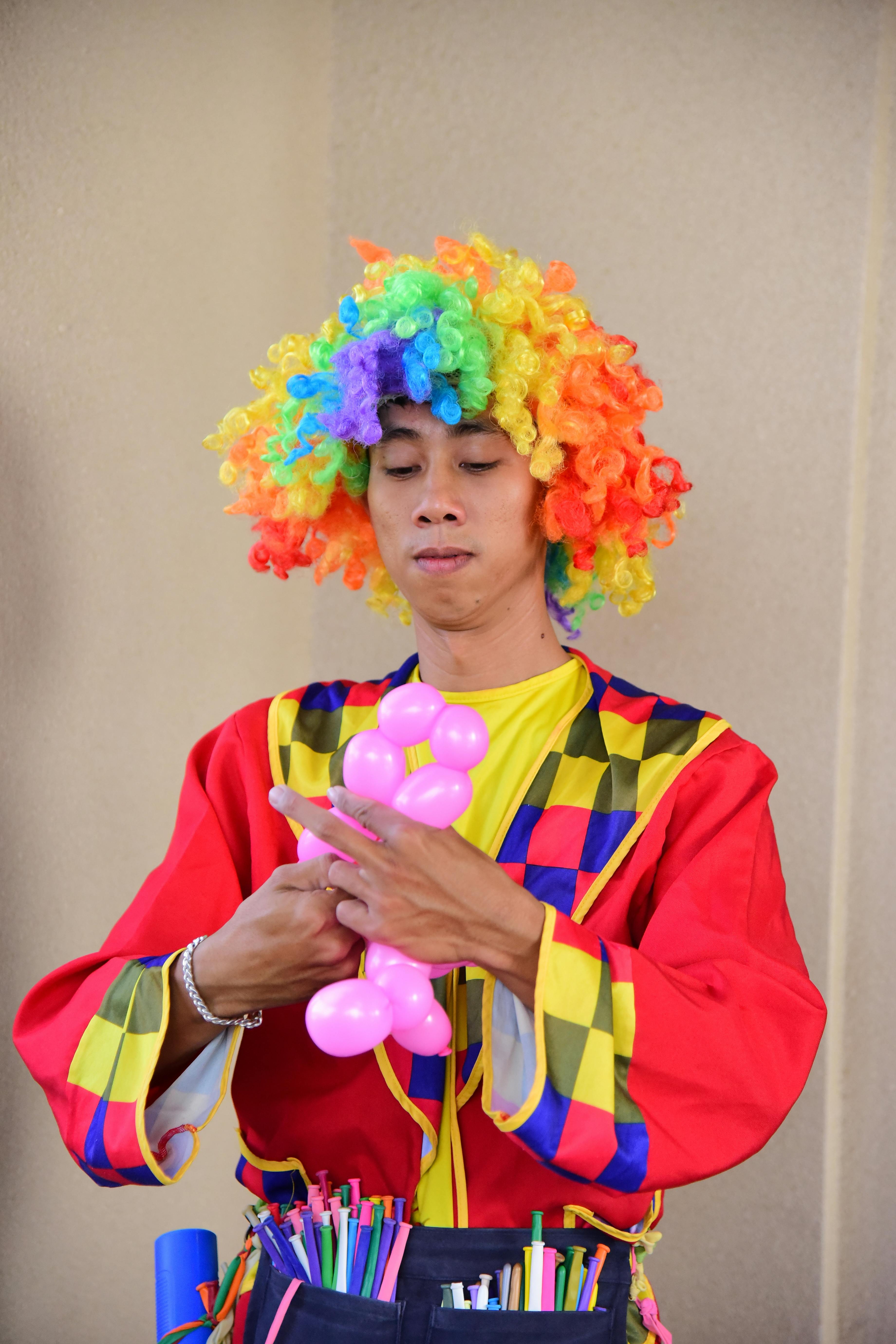 Gratis Badut berpakaian warna-warni membuat hewan dari balon di dalam ruangan, menangkap esensi perayaan. Foto Stok