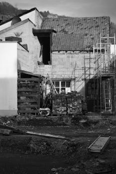 A black and white image of a rustic building under renovation with construction materials.