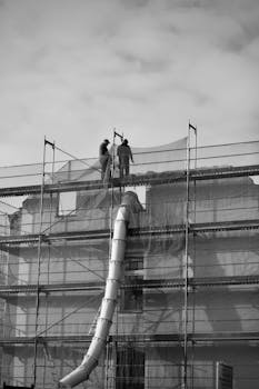 Two workers standing on scaffolding at a construction site in black and white.