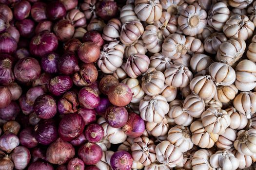 Top view of red onions and garlic bulbs side by side, highlighting textures in a Vietnamese market.