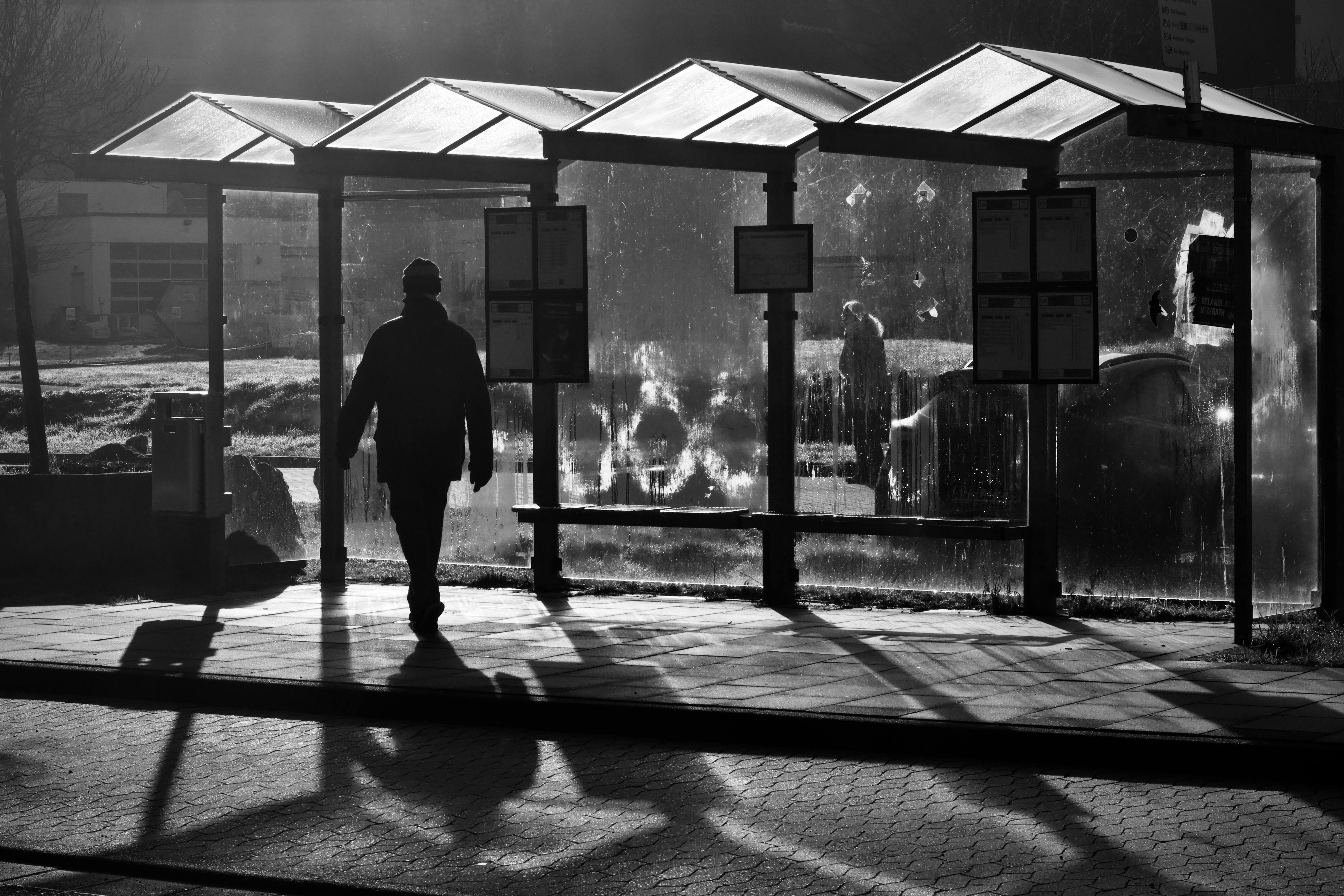 無料 シルエットになった男性がバス停でバスを待ち、都会の風景に影を落としている。 写真素材