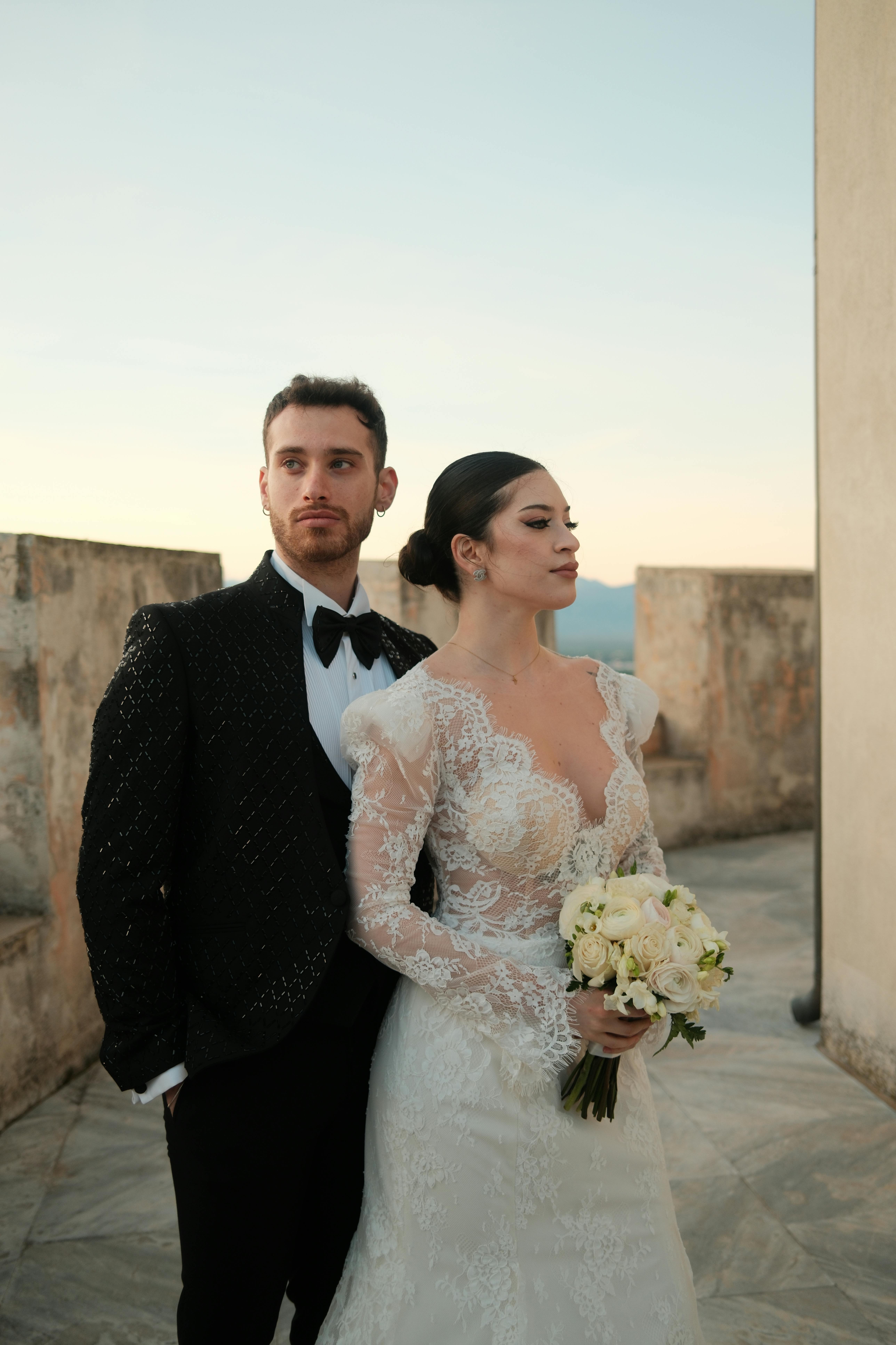 Gratis Et par i formelle bryllupsantrekk poserer grasiøst på et tak under solnedgang, og viser frem eleganse og romantikk. Arkivbilde