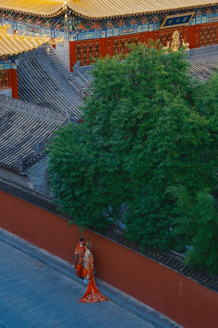 Couple in traditional attire near Chinese temple wall, seen from above.