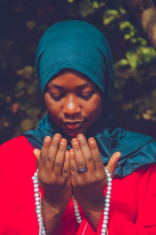 Free A young woman wearing a hijab prays outdoors holding prayer beads. Peaceful and spiritual atmosphere. Stock Photo