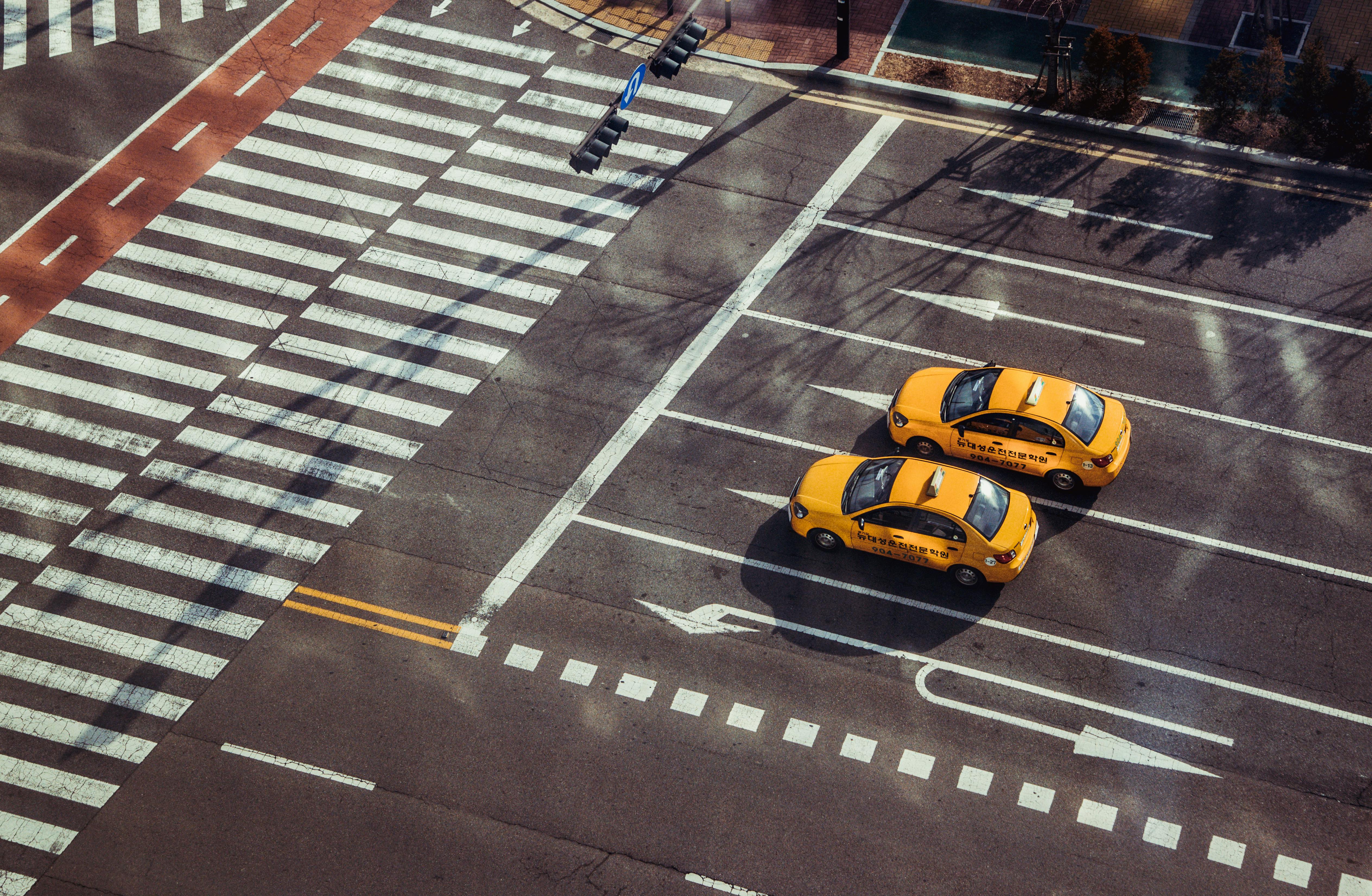 Two yellow taxis navigate a city intersection with marked pedestrian crossings.