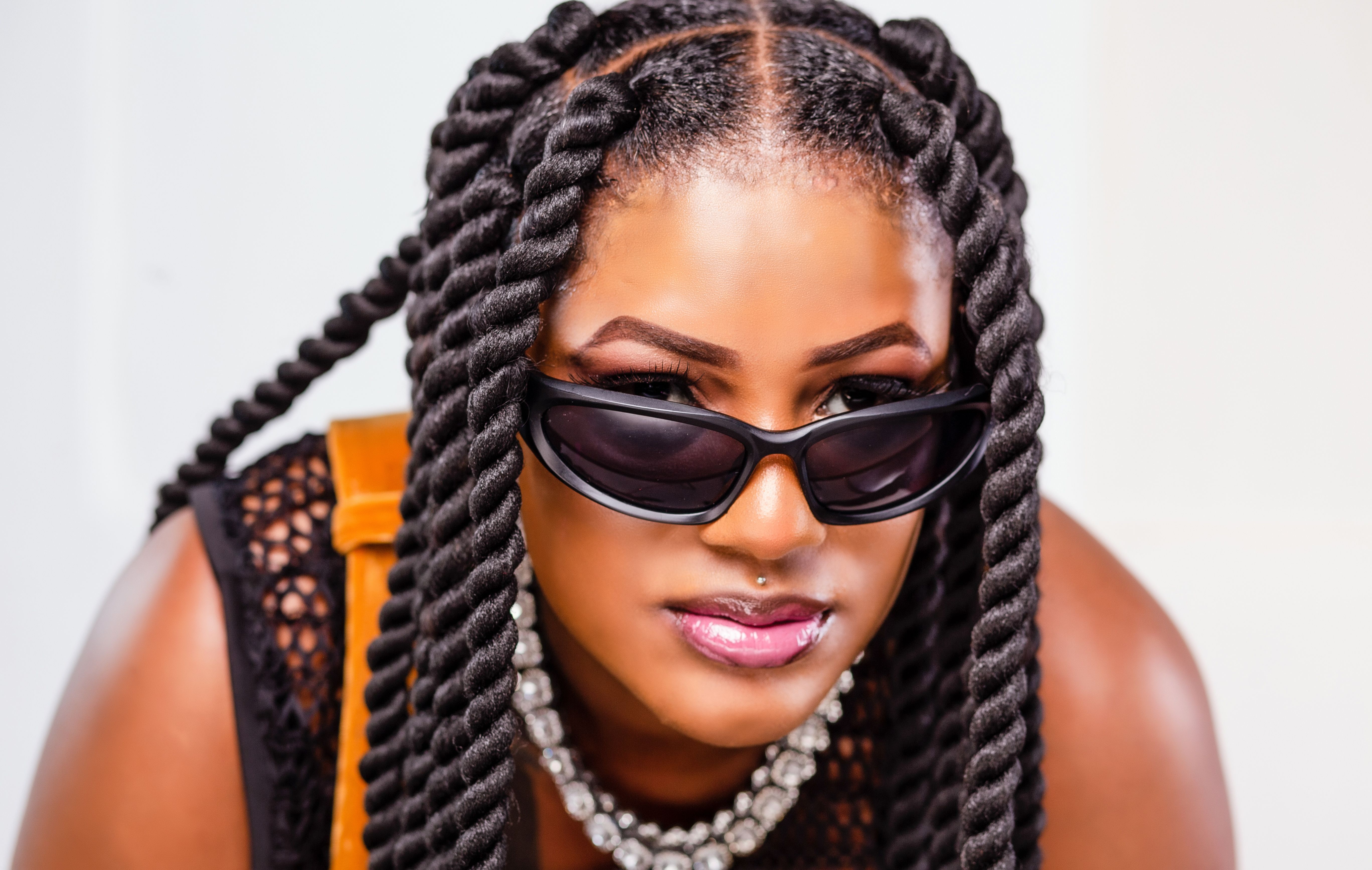 Close-up portrait of a fashionable woman with sunglasses and twisted hairstyles, exuding confidence.