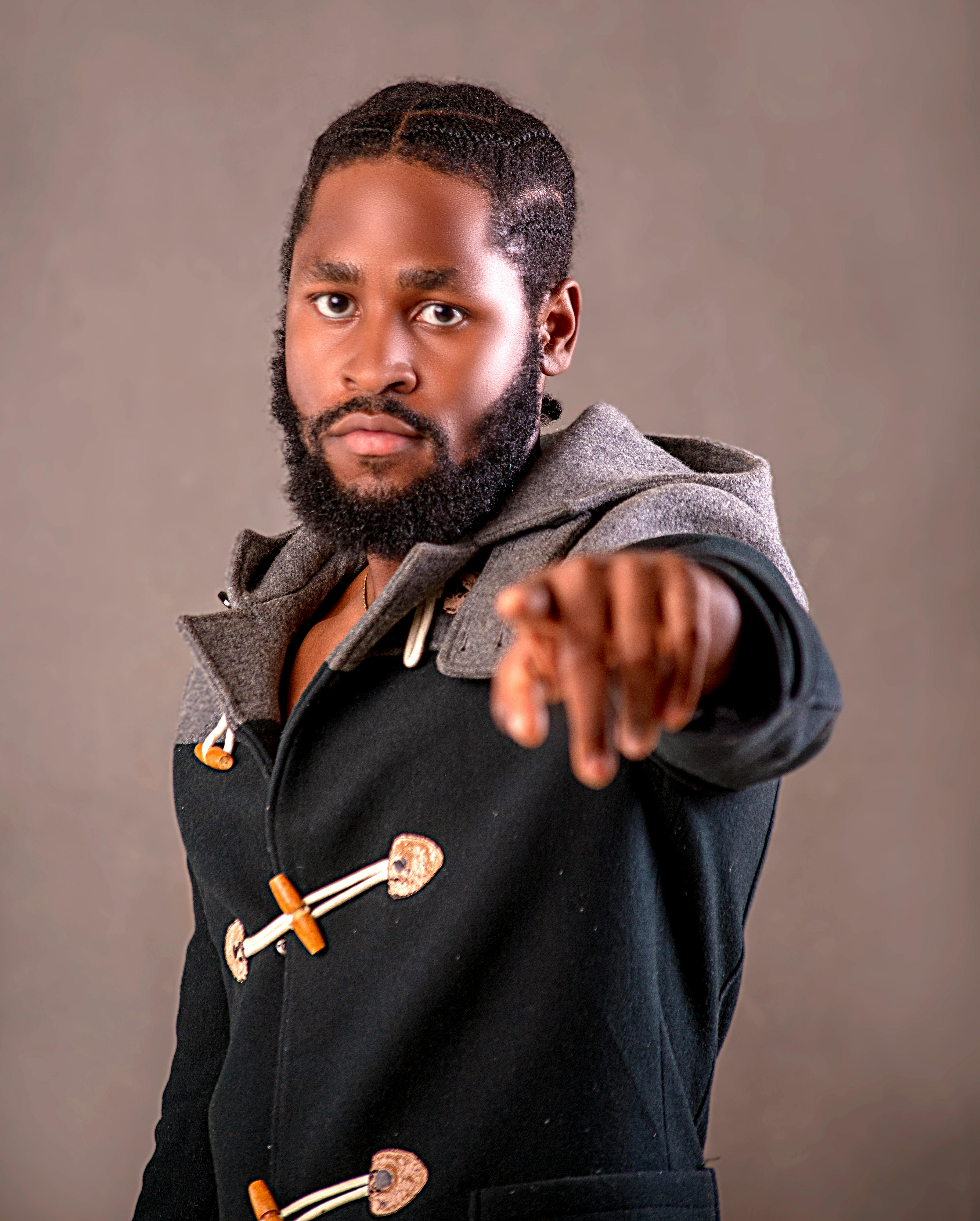 Portrait of a confident man pointing at the camera, wearing a modern, stylish coat. Studio lighting enhances the bold expression.
