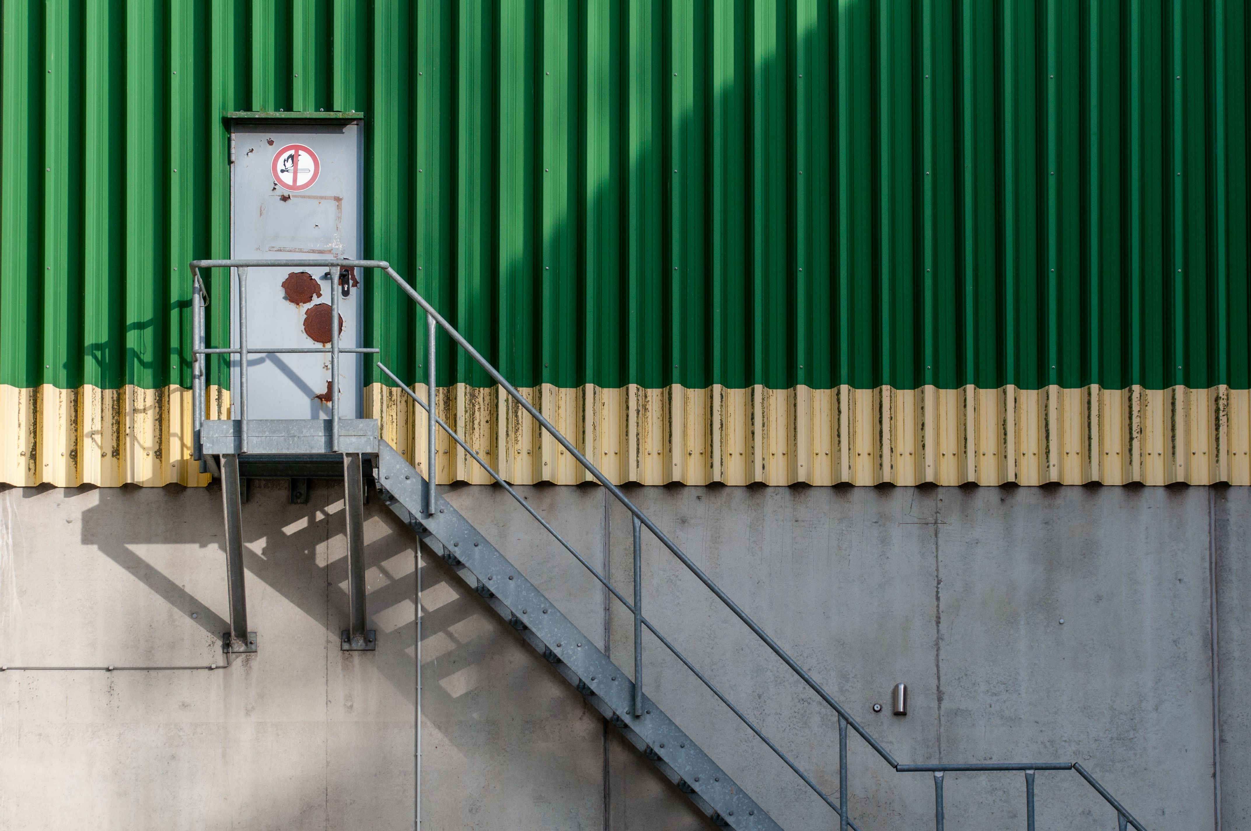 Imagem de uma porta de emergência instalada na parede de uma construção industrial com escada de acesso externo.