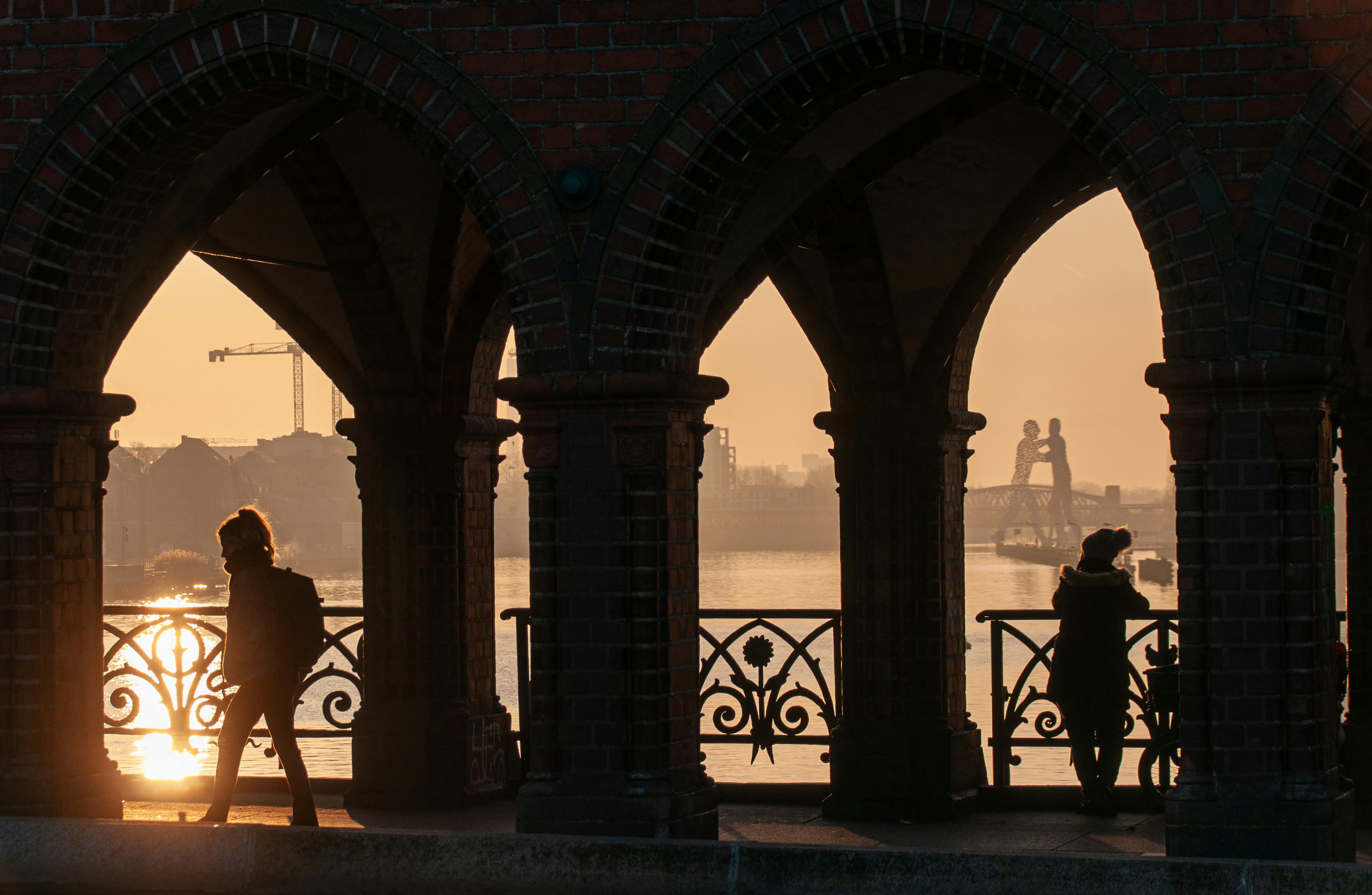 Gratis Siluet sosok-sosok di Jembatan Oberbaum saat matahari terbenam yang tenang di Berlin, Jerman. Foto Stok