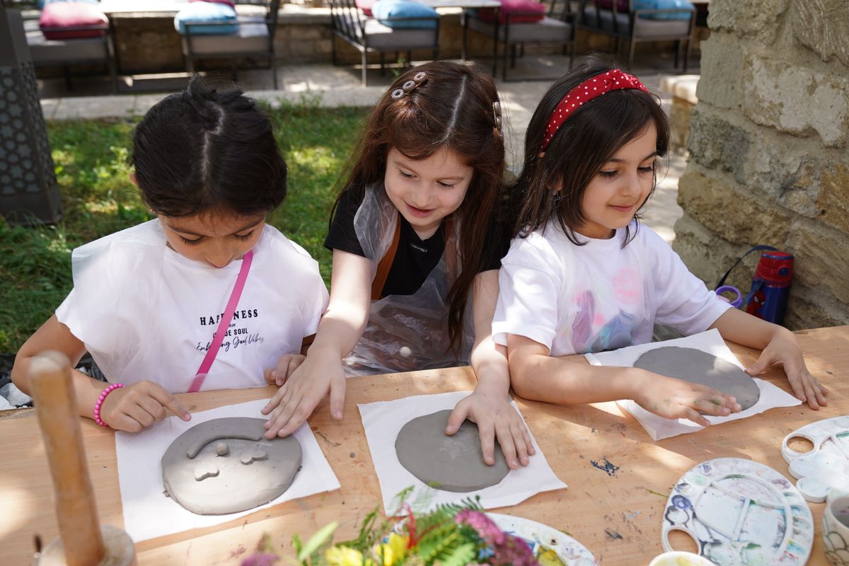Three children crafting with clay outdoors on a sunny day