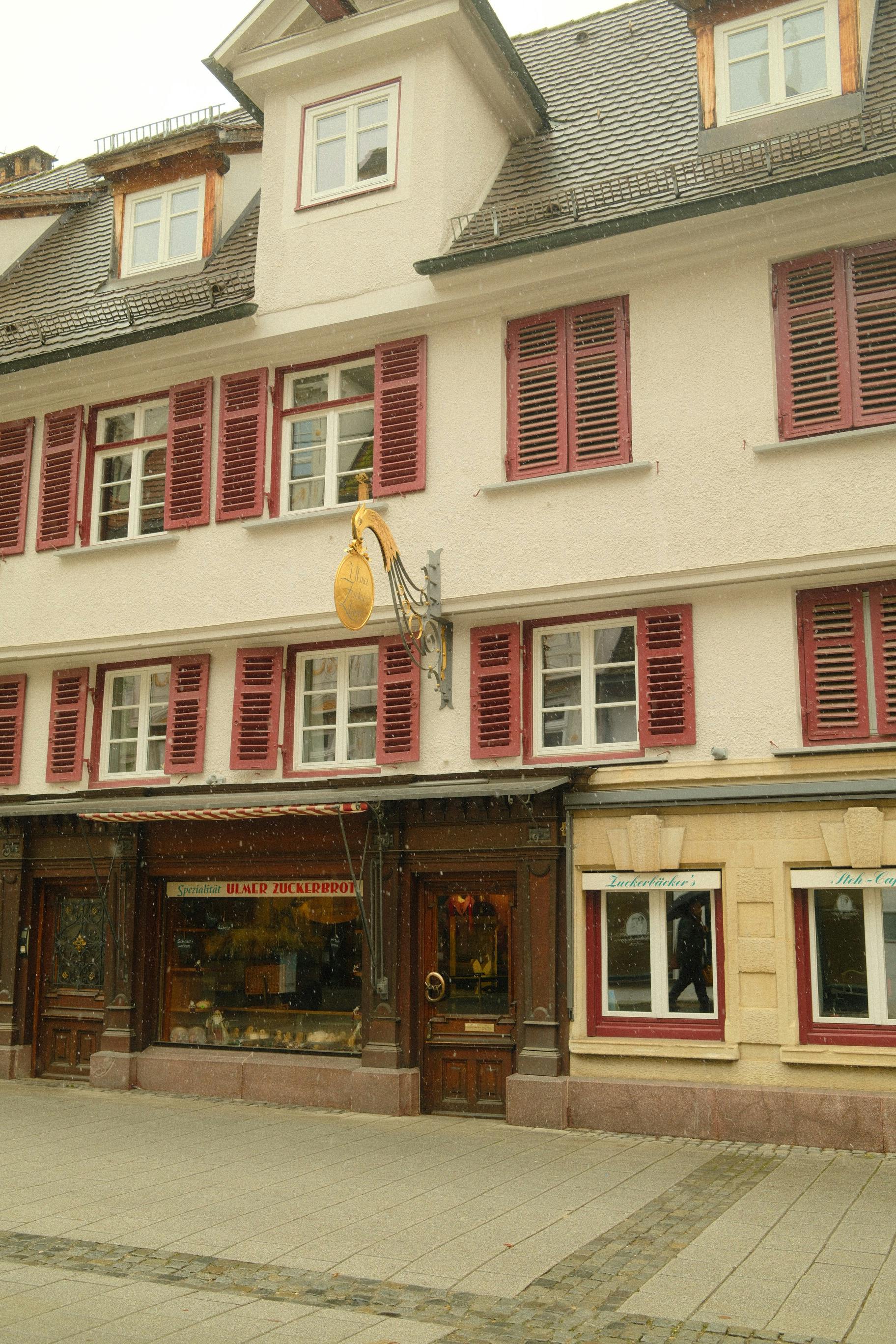 無料 ドイツのウルムにある、赤いシャッターとユニークな看板が付いた伝統的な建物のファサード。 写真素材
