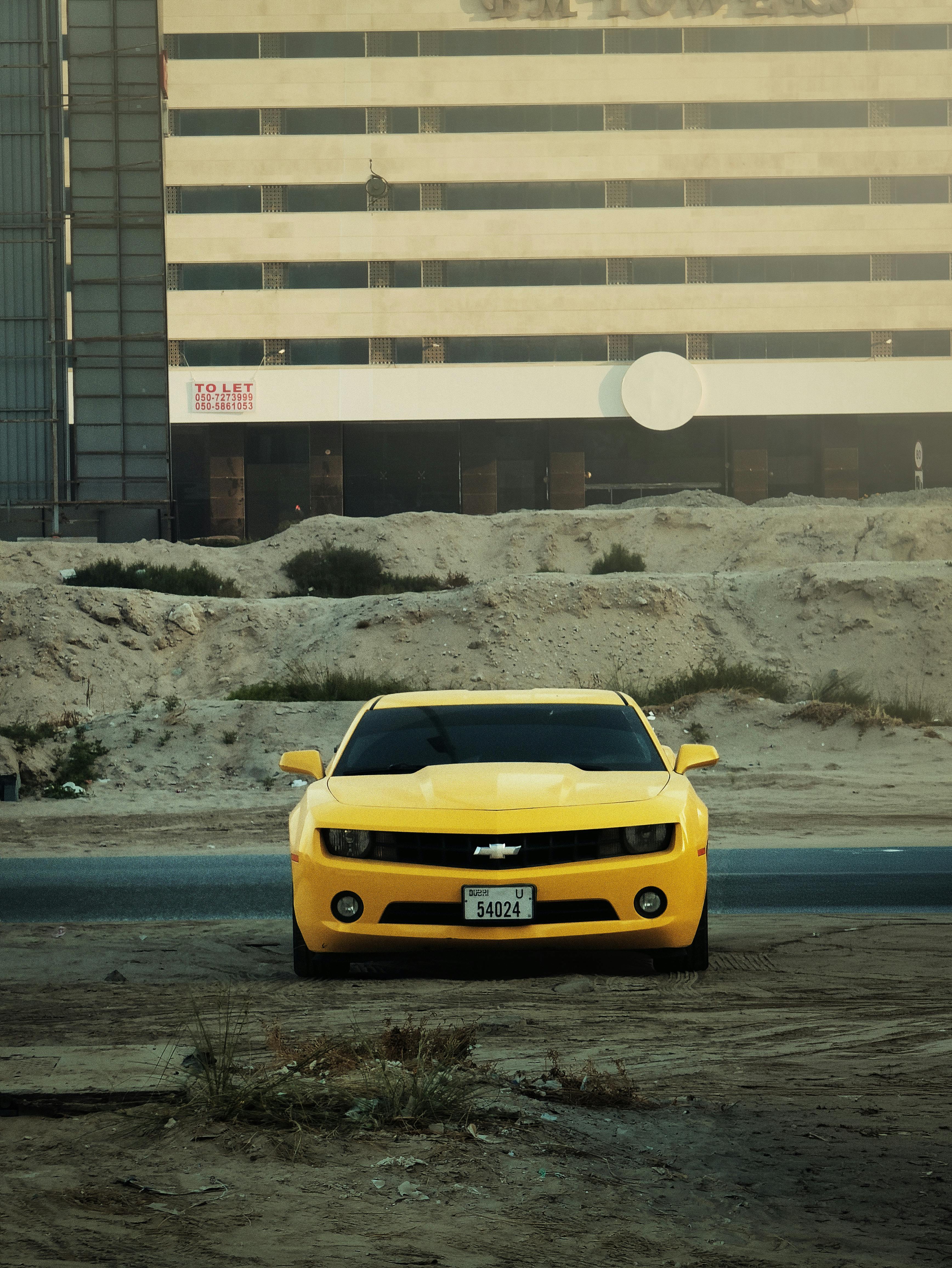 бесплатная Желтый спортивный автомобиль припаркован снаружи на фоне современного здания. Стоковое фото