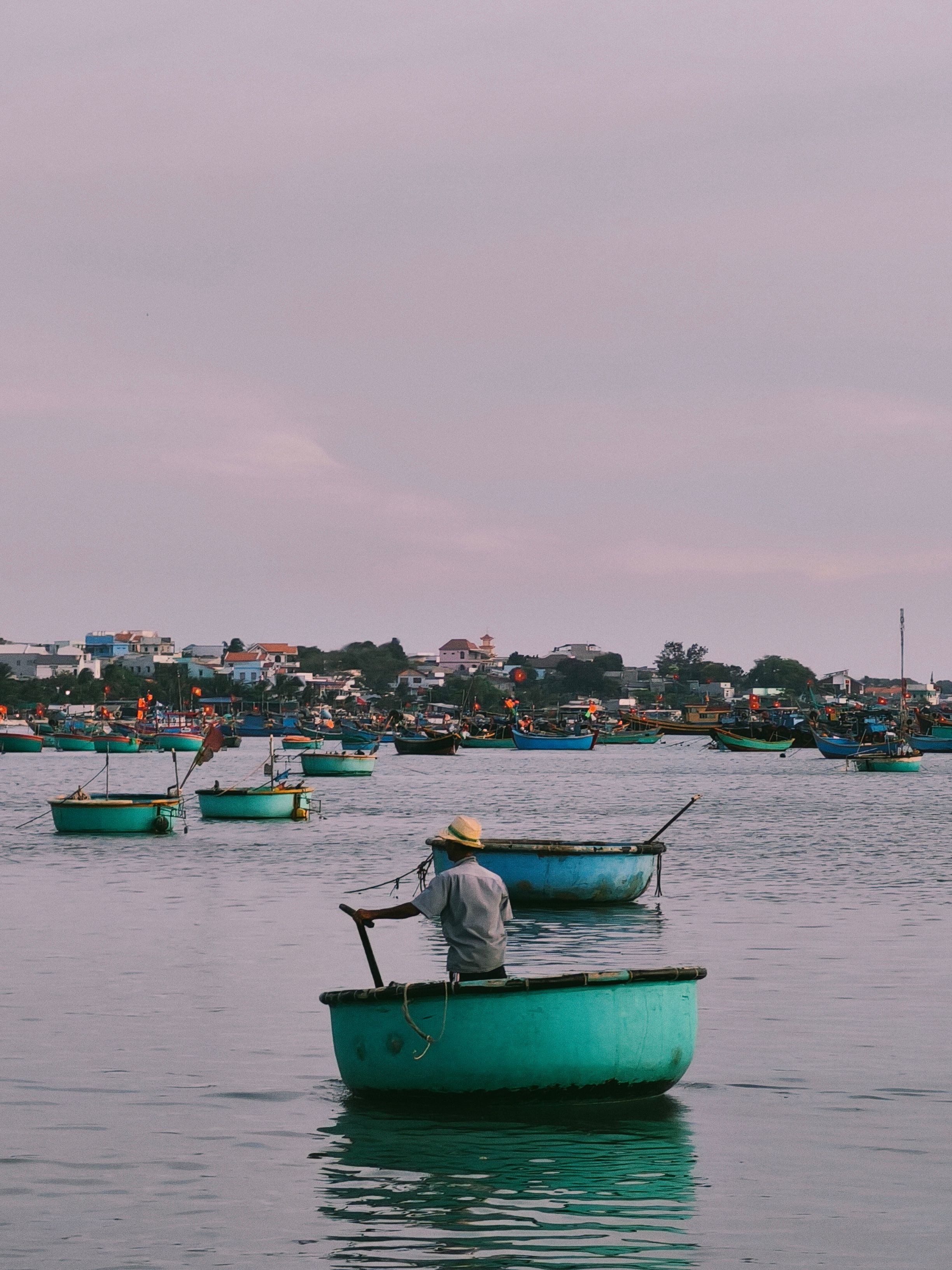 Man rowing a round basket boat on calm waters with coastal village view. Idyllic fishing scene.