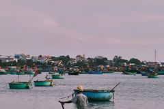 Man rowing a round basket boat on calm waters with coastal village view. Idyllic fishing scene.