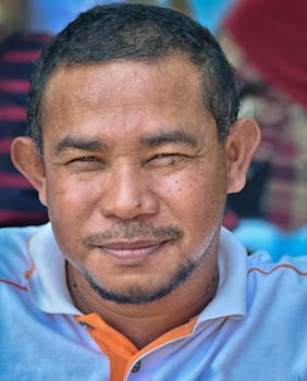 Close-up portrait of a smiling middle-aged man with a beard and short hair, wearing a casual shirt outdoors.