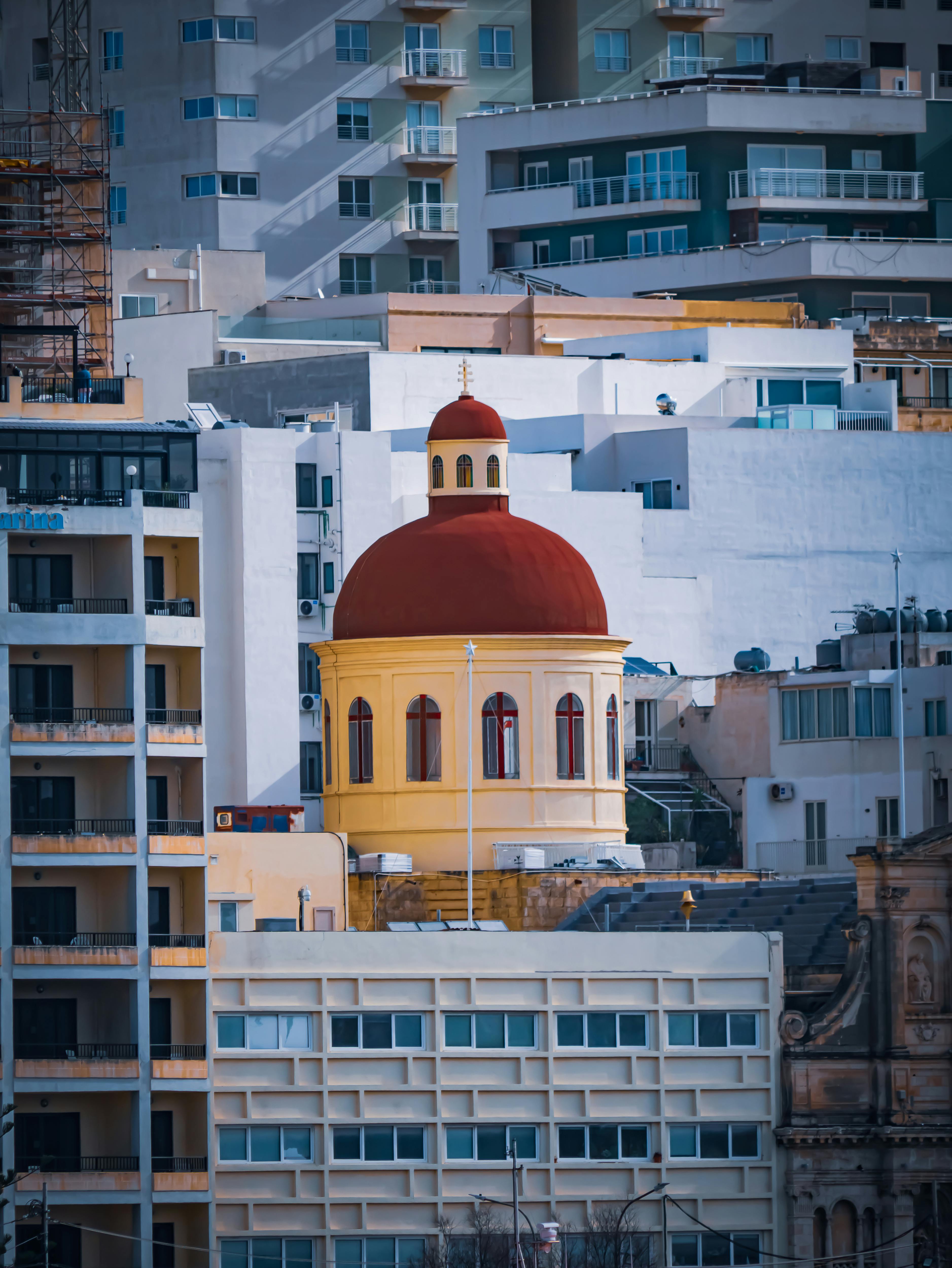 無料 マルタの近代的な建物に囲まれた印象的な赤いドーム。建築のコントラストが際立っています。 写真素材