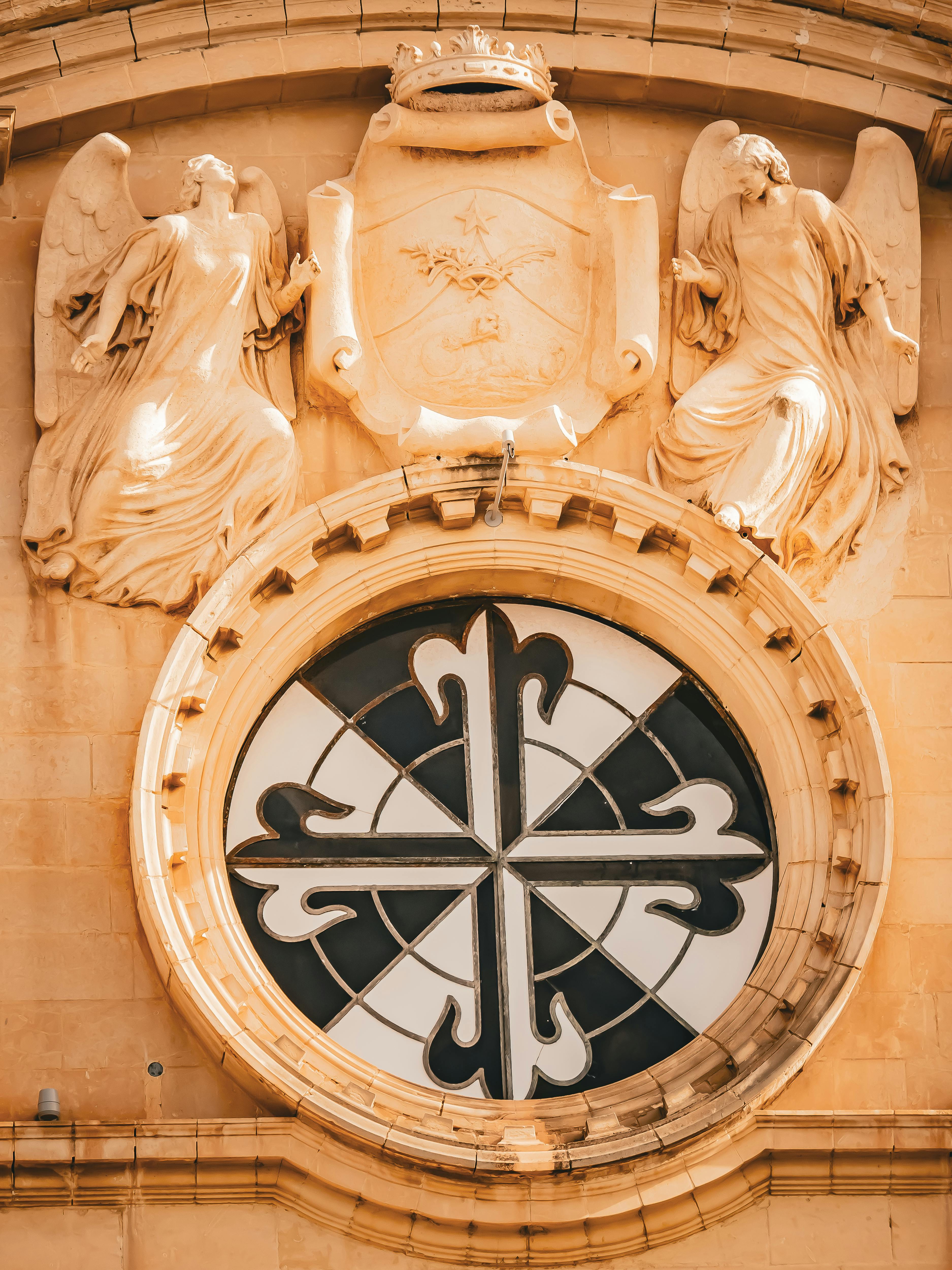 бесплатная Крупный план замысловатой резьбы по камню и круглого витражного окна исторической мальтийской церкви. Стоковое фото