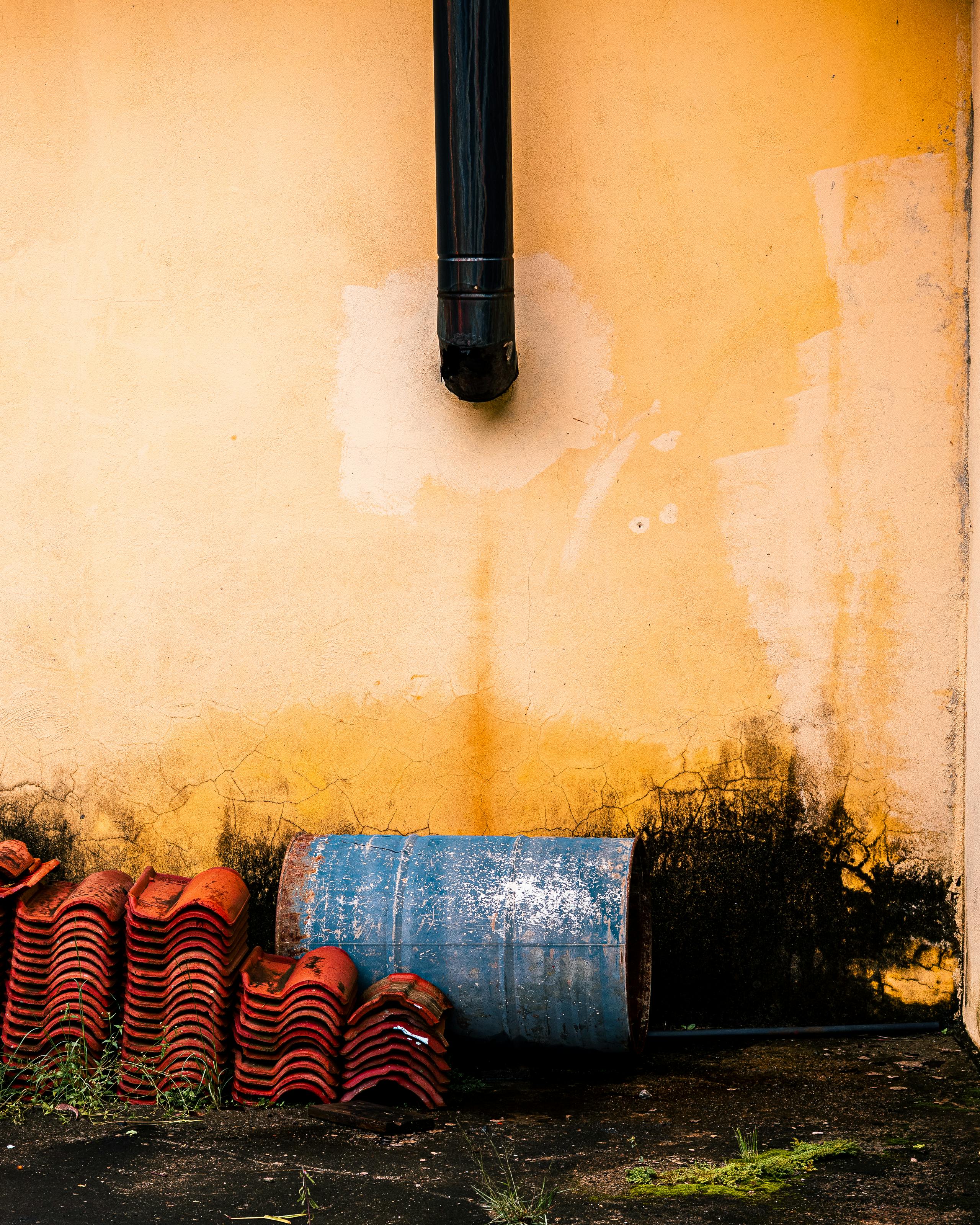 бесплатная На обветшалой стене видны синяя бочка, черная водосточная труба и сложенная красная черепица. Стоковое фото