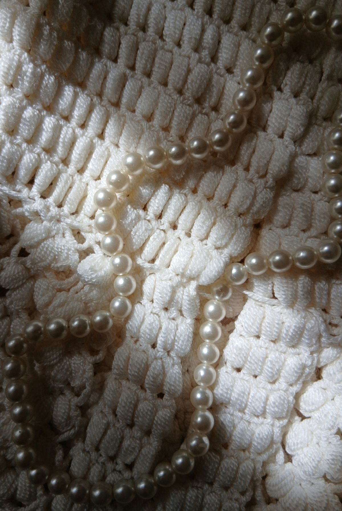 A pearl necklace resting on crochet fabric — the texture up close