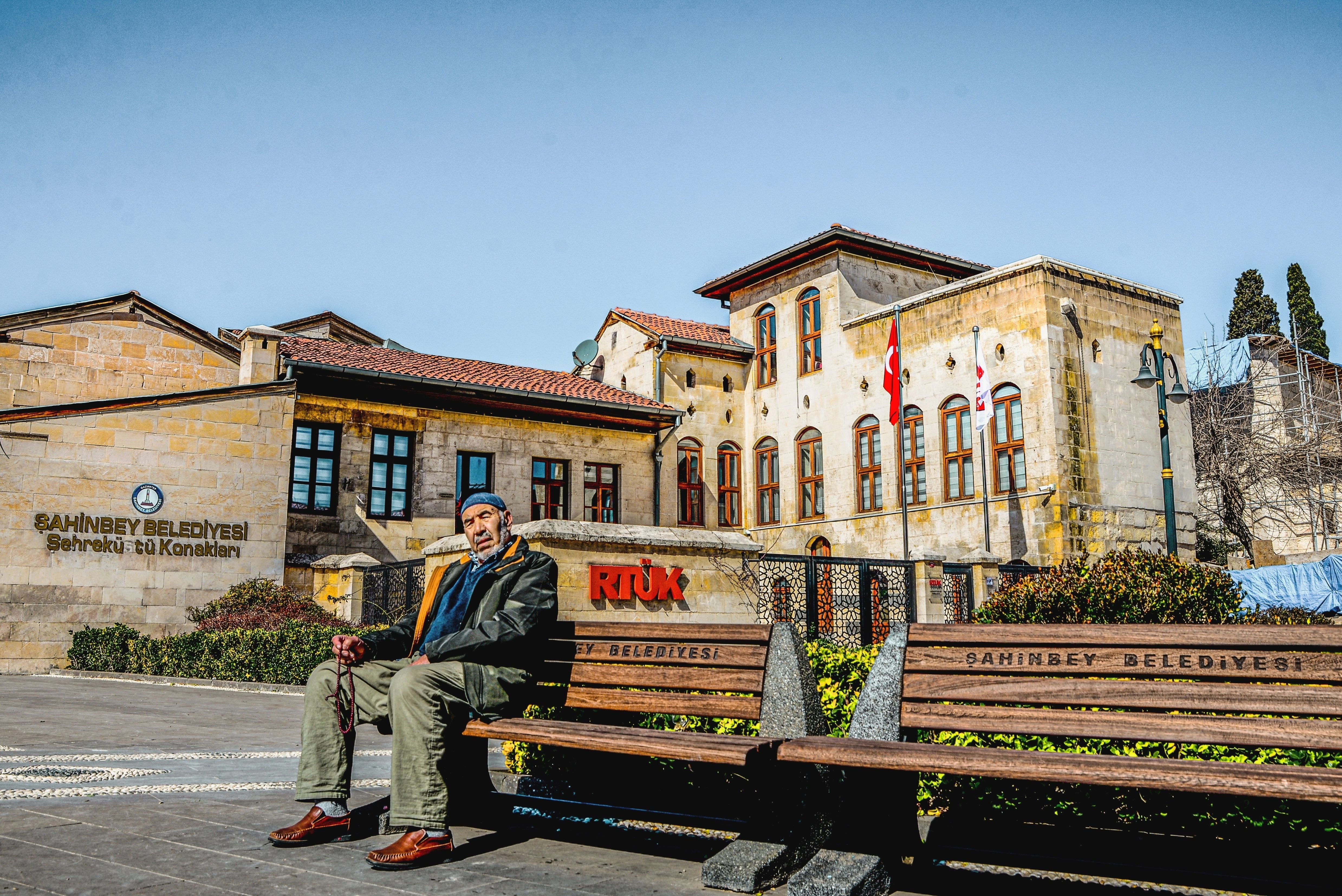 Elderly man sitting on a bench outside Şahinbey Municipality building in Gaziantep, Turkey.