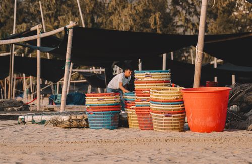Free A person organizes vibrant baskets on a sunlit beach. Outdoor market scene. Stock Photo