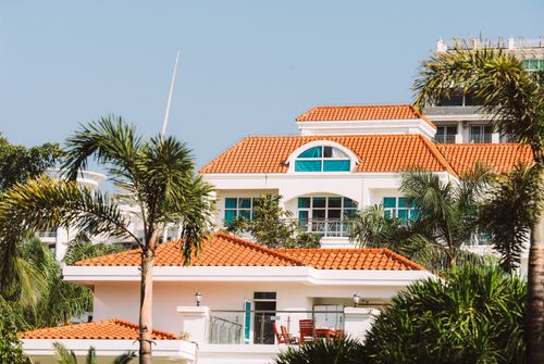 Free A stunning villa featuring Mediterranean architecture with orange roof tiles and lush palm trees. Stock Photo