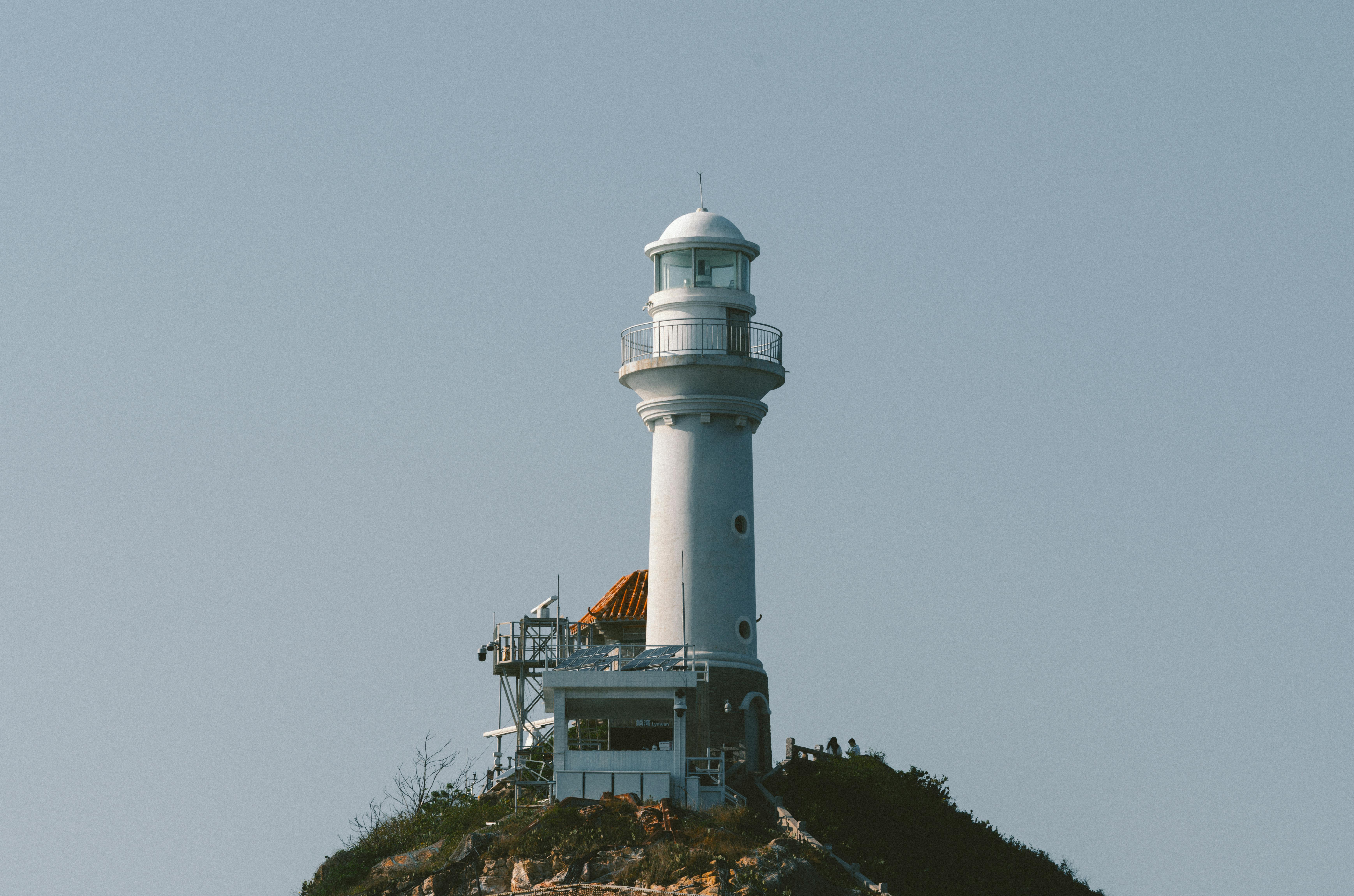 無料 澄み切った青い空を背景に、岩だらけの崖の上に建つ印象的な白い灯台。導きと安全を象徴しています。 写真素材